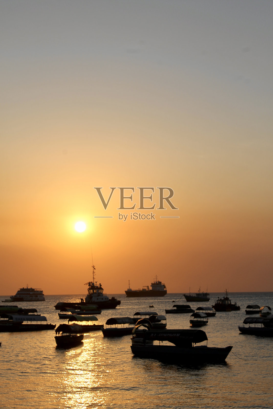 在桑给巴尔的石头镇港口，充满活力的橙色太阳落在停泊的船只上照片摄影图片