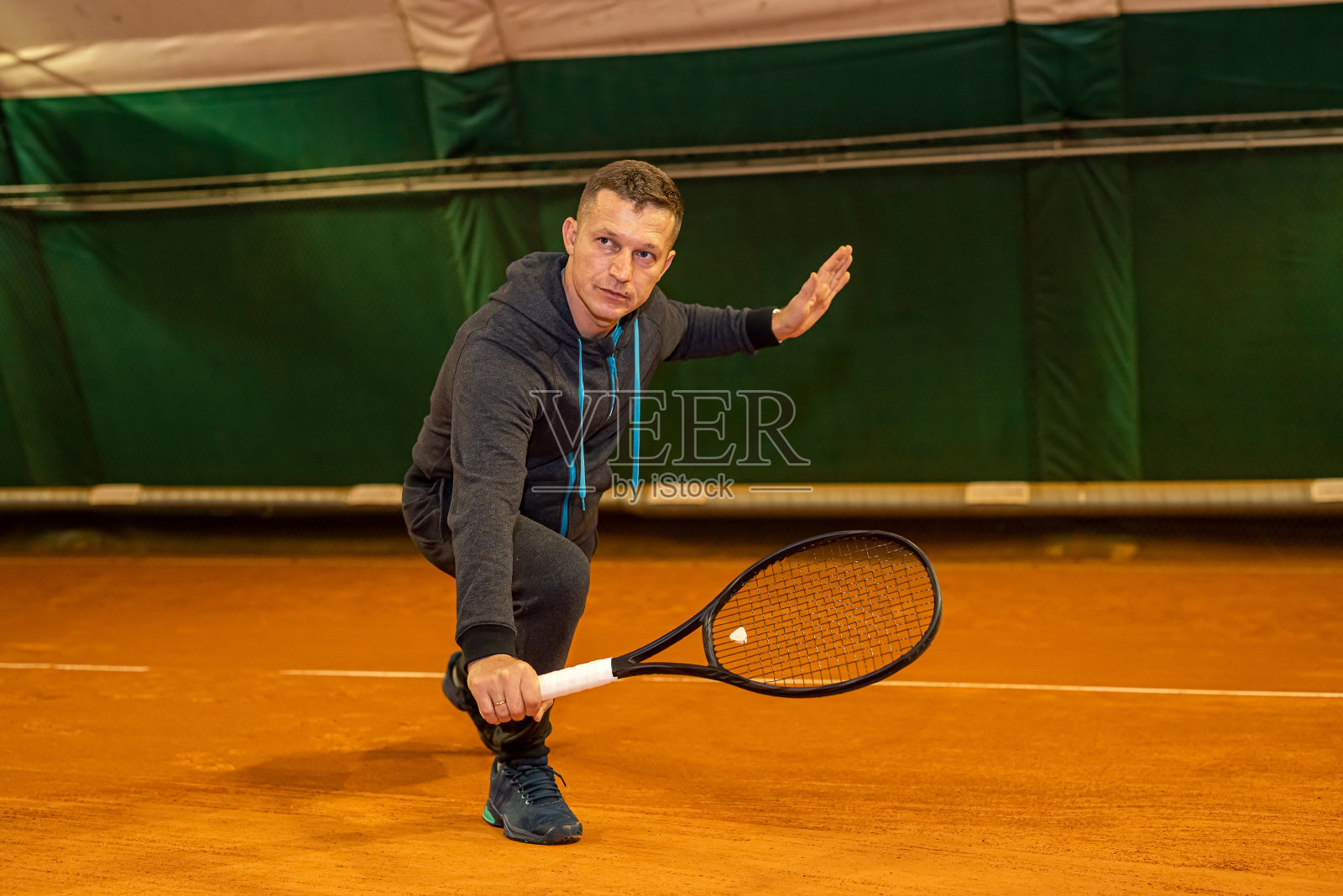 一名男子在有网的室内球场上用球拍和球打网球。照片摄影图片
