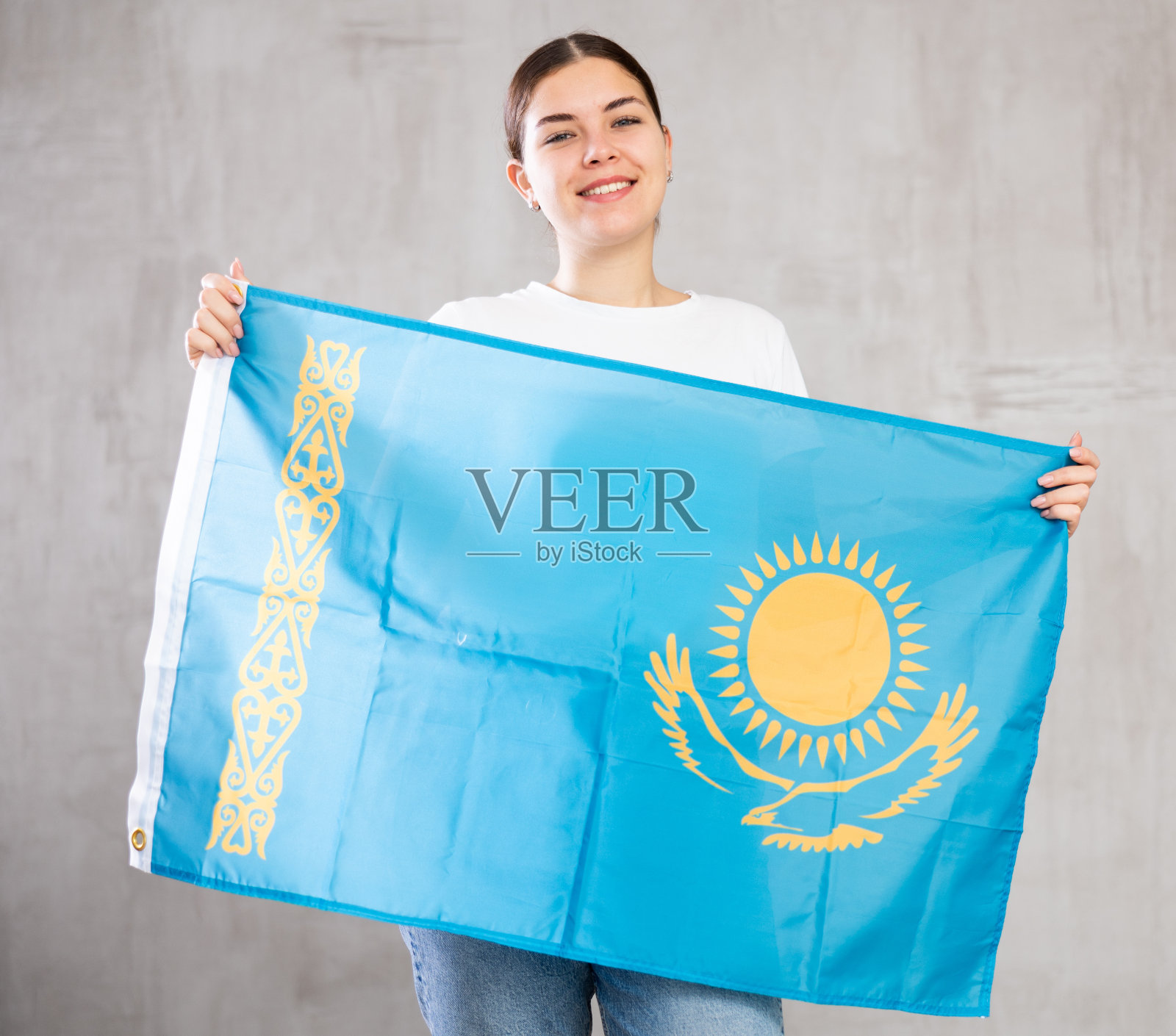 快乐的年轻女子在室内灰色背景下手持哈萨克斯坦国旗照片摄影图片