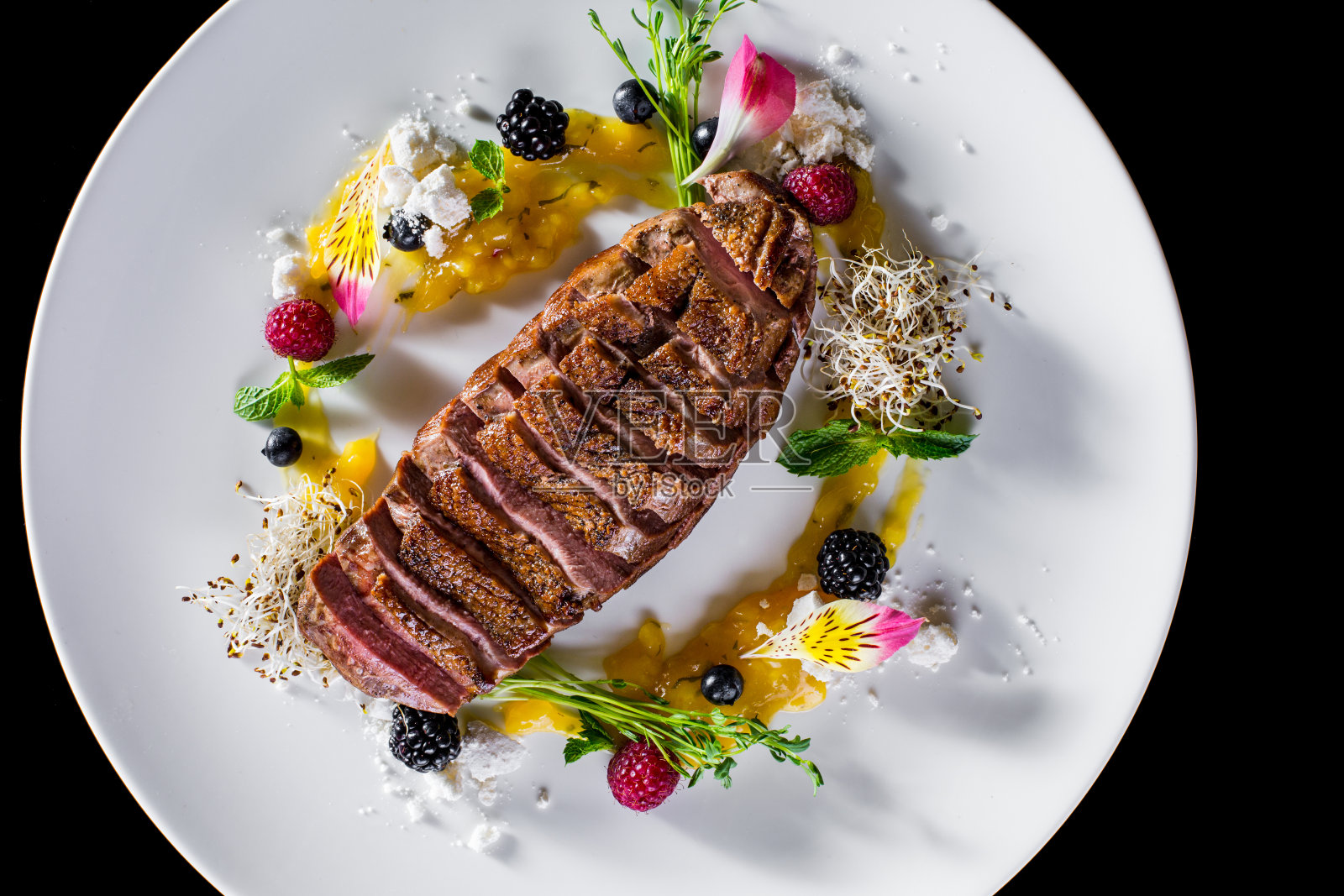 烤切好的鸭胸肉，配上果酱、黑莓、覆盆子、醋栗、薄荷、嫩枝和花瓣，放在白色盘子和深色背景上。水平方向照片摄影图片