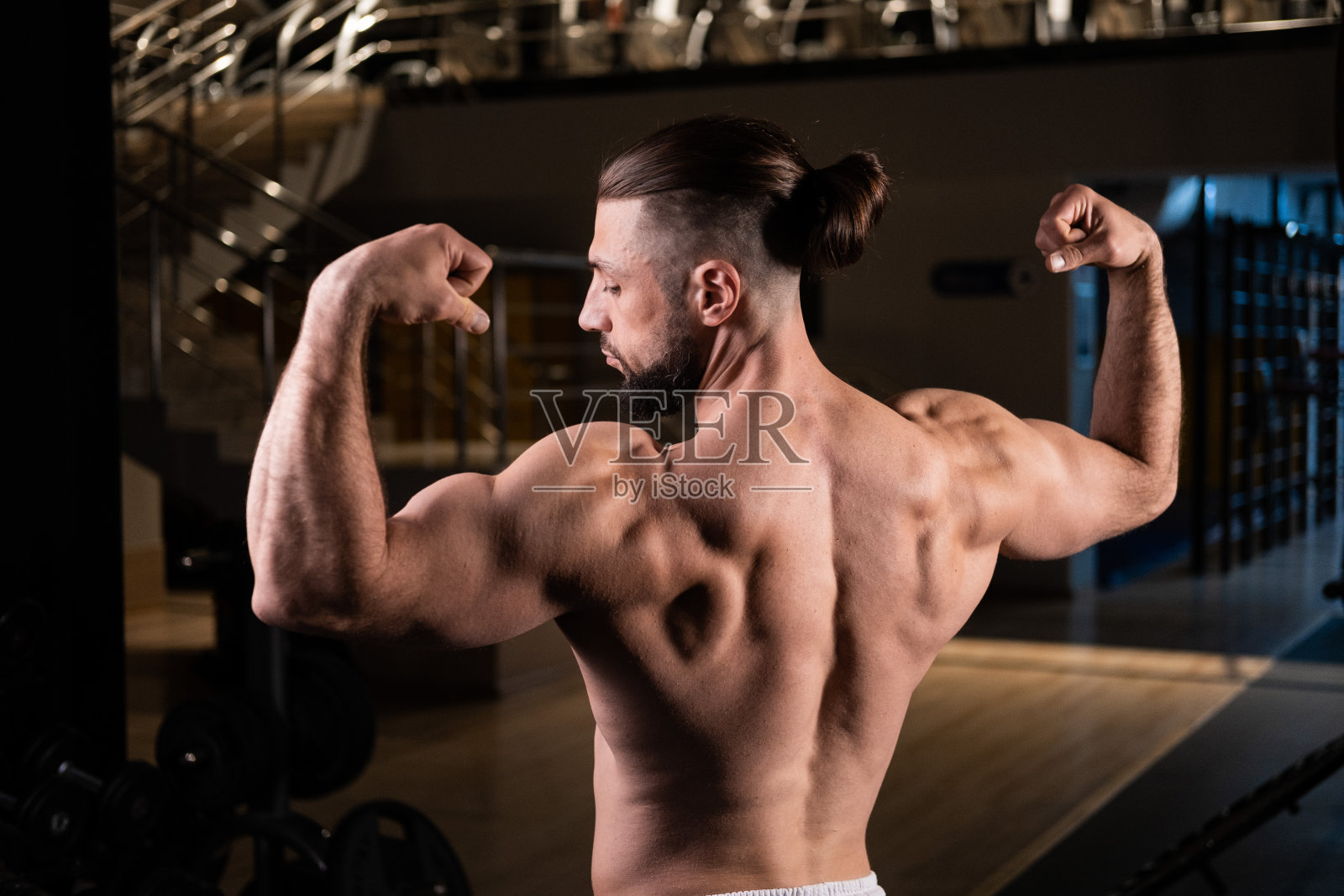一位英俊的大胡子男运动员，肌肉发达，在健身房摆姿势，展示他的肱二头肌和背部照片摄影图片