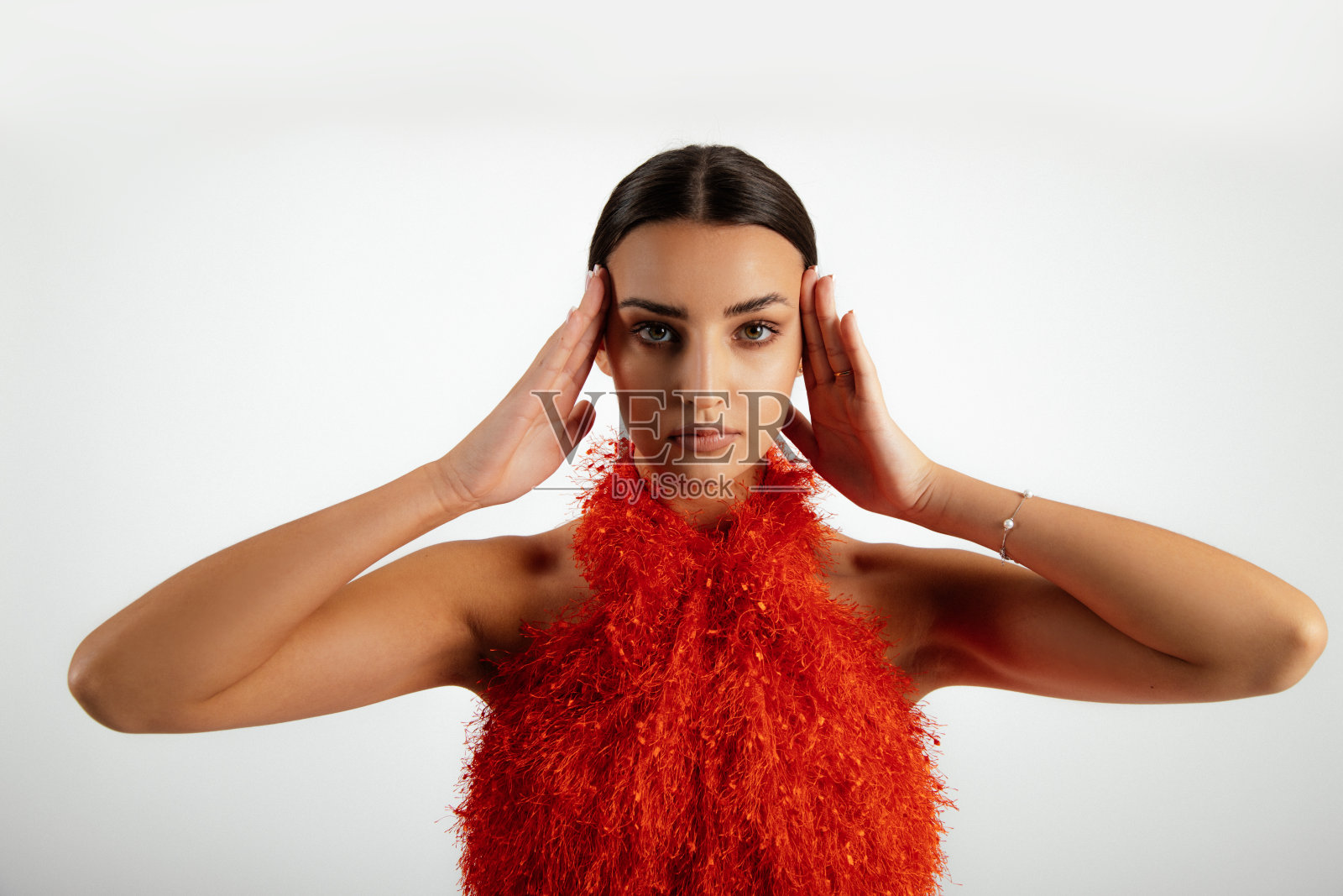 特写严肃。时髦的深色头发的女人化妆在橙色连衣裙与衣领pose与手在太阳穴，看相机照片摄影图片