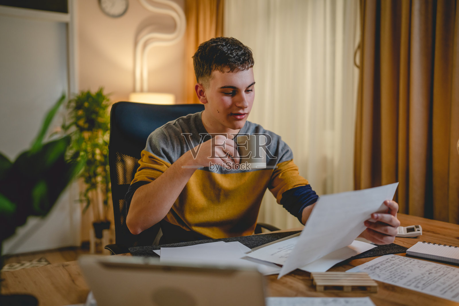 年轻的白人男子，十几岁的学生，晚上在家里的桌子上学习照片摄影图片