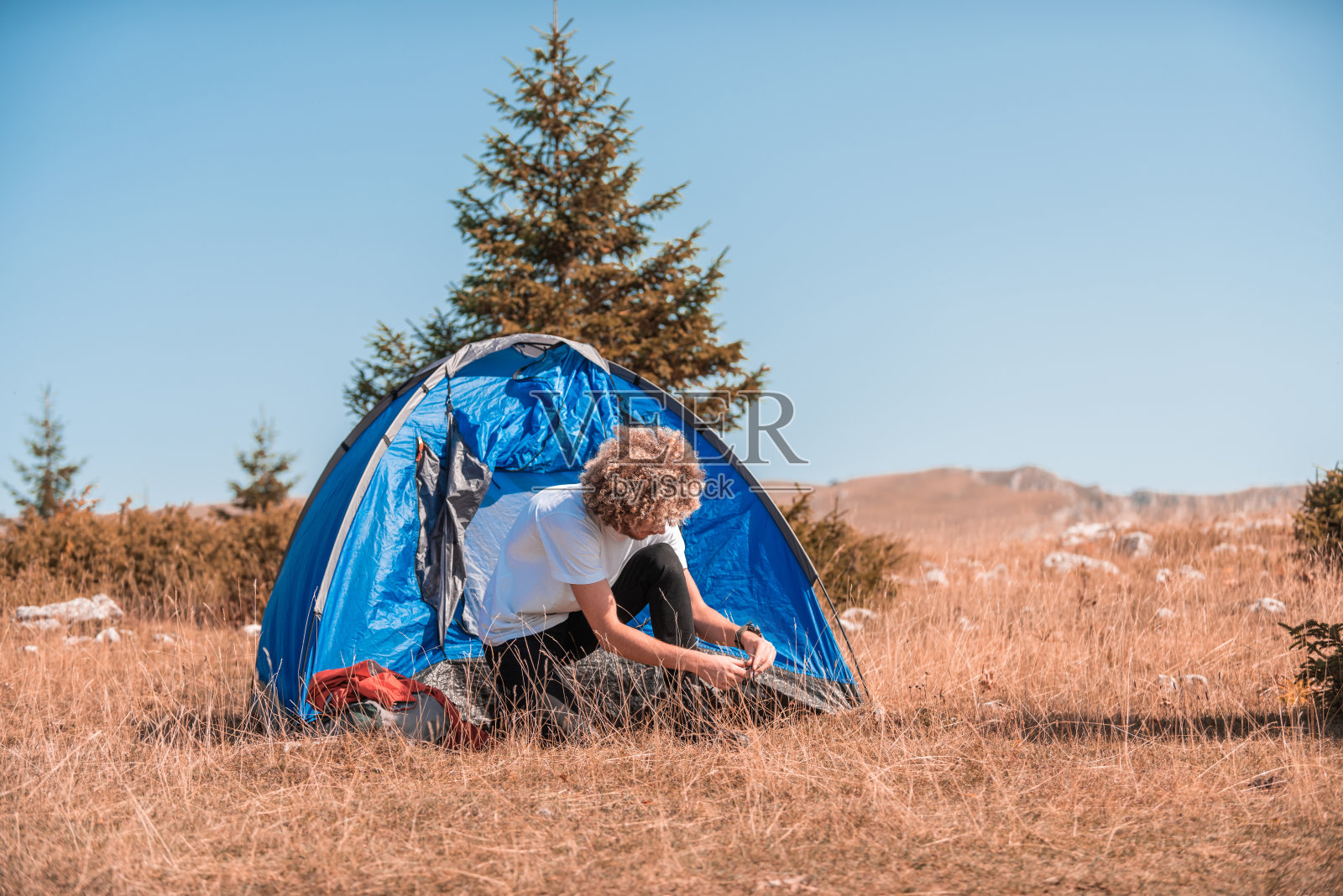 带着帐篷露营的男人。他被美丽的山景包围着，阳光照在他的脸上，预示着美好的阳光灿烂的一天。这名男子看起来很满足，表明他很享受这次冒险之旅。照片摄影图片