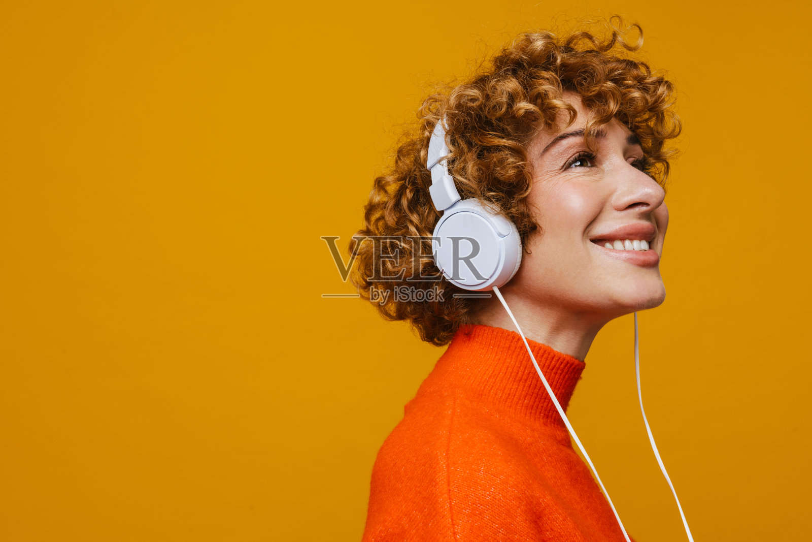卷发姜女人戴着耳机微笑着听音乐照片摄影图片