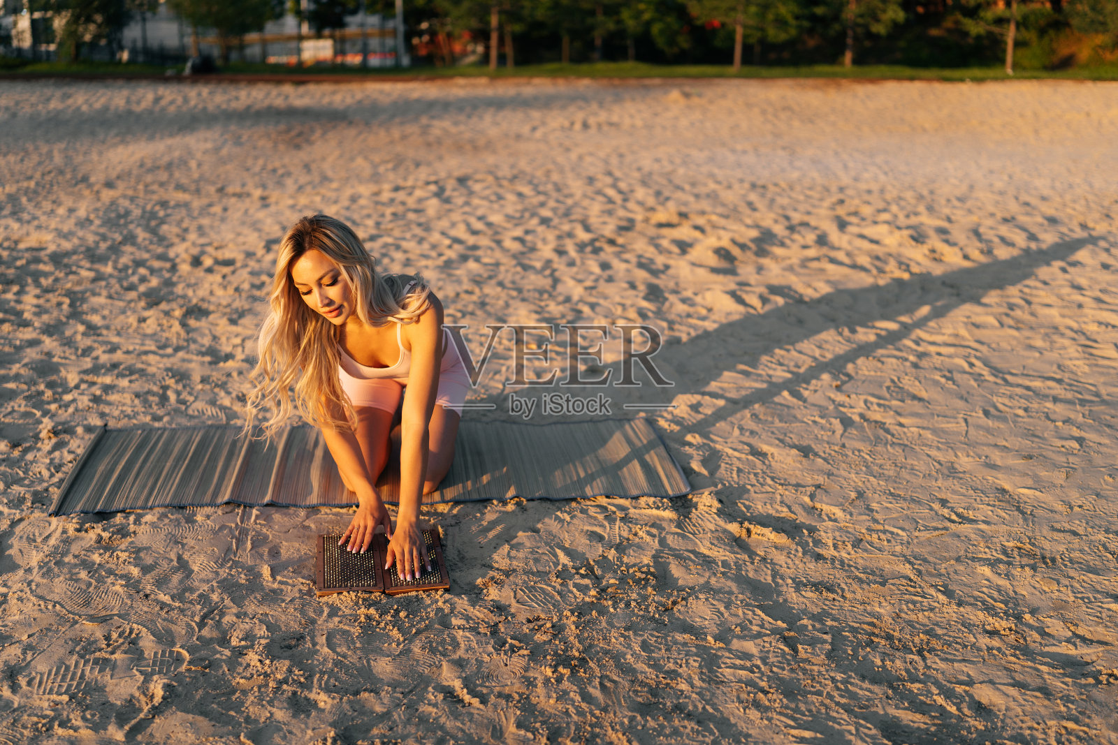 前视图的年轻女子持有Sadhu板与指甲在手中和触摸尖锐的指甲与手掌在沙滩上的夏天阳光灿烂的一天。照片摄影图片