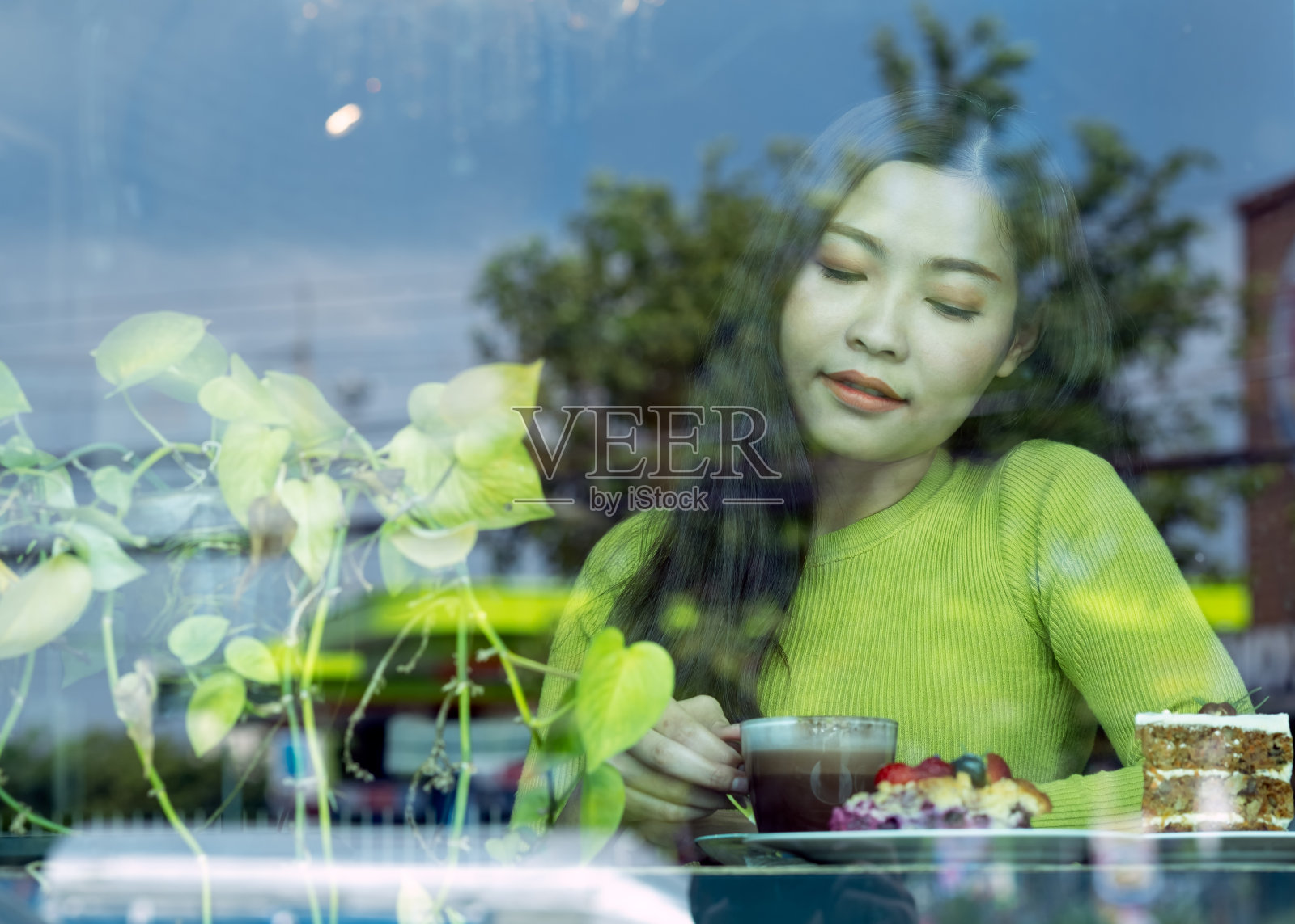 亚洲美丽的年轻女子在绿色毛衣热拿铁咖啡坐在咖啡馆窗口照片摄影图片