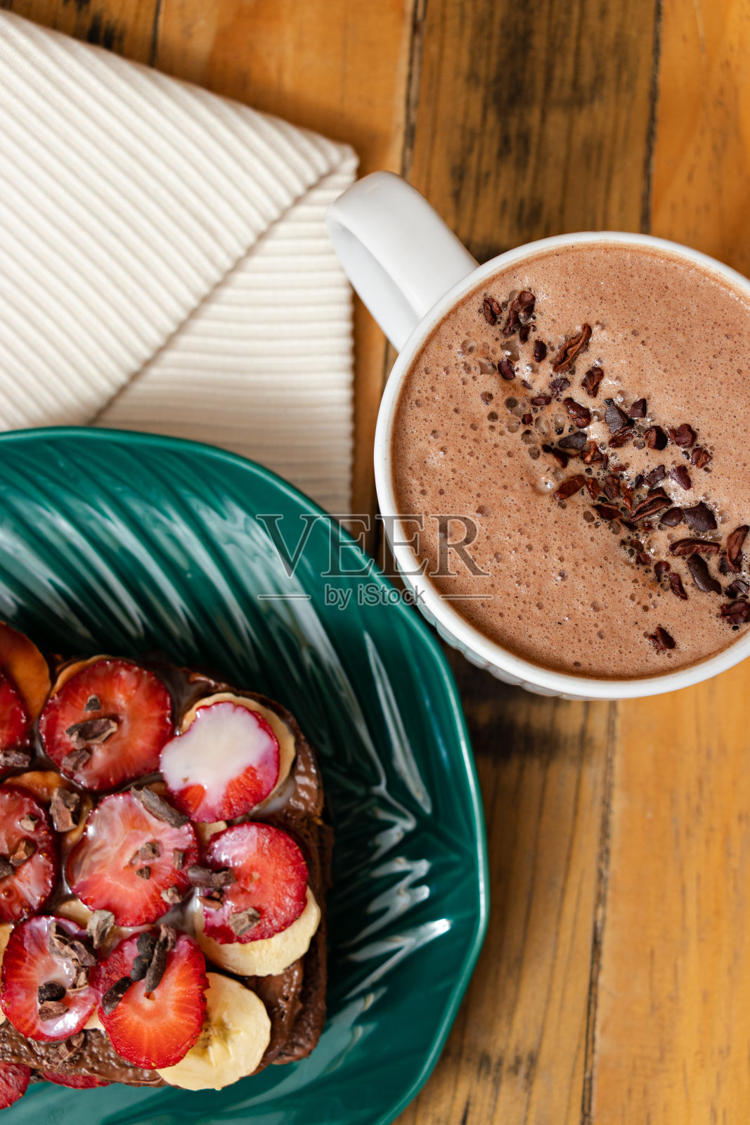 头顶上的一个盘子，上面有切片面包和水果配料，旁边还有一杯闪闪发光的巧克力照片摄影图片