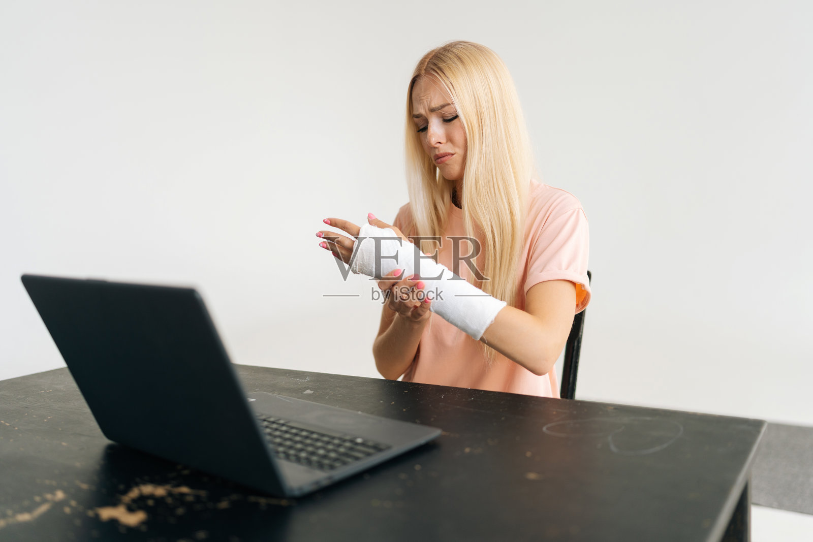 沮丧的金发年轻女子的肖像骨折的手臂包裹在石膏绷带有视频通话，使用笔记本电脑在线咨询。照片摄影图片