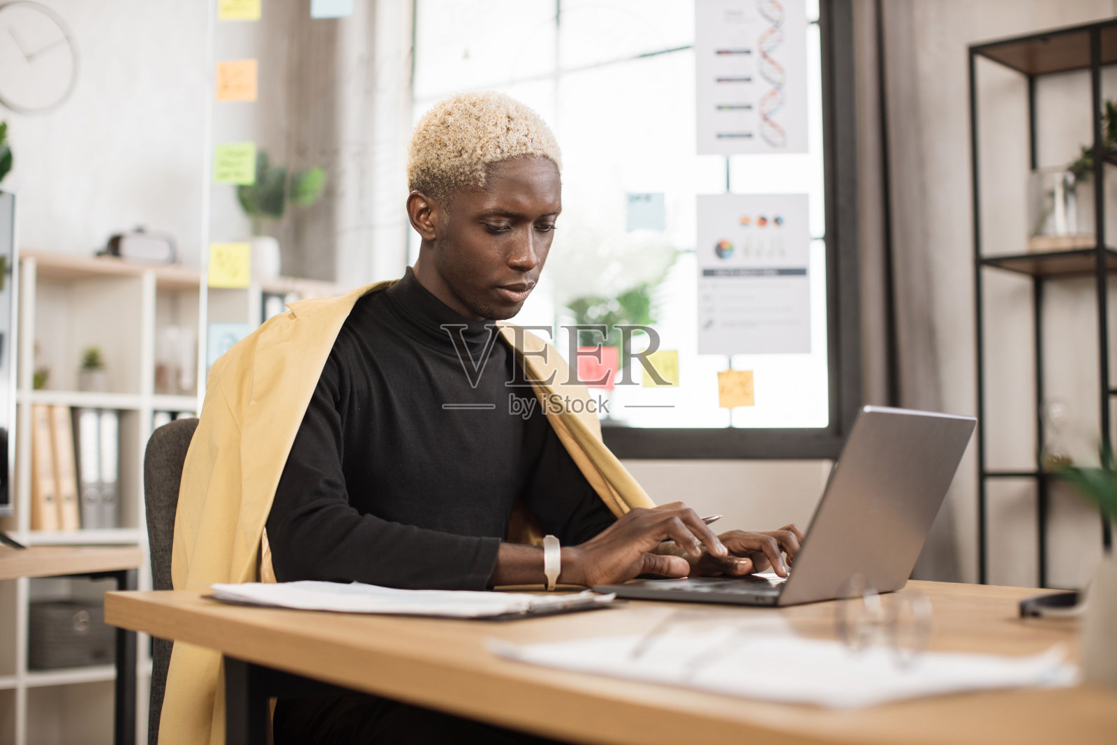 成功的非洲商人在时尚的西装在笔记本电脑在现代办公室工作。照片摄影图片