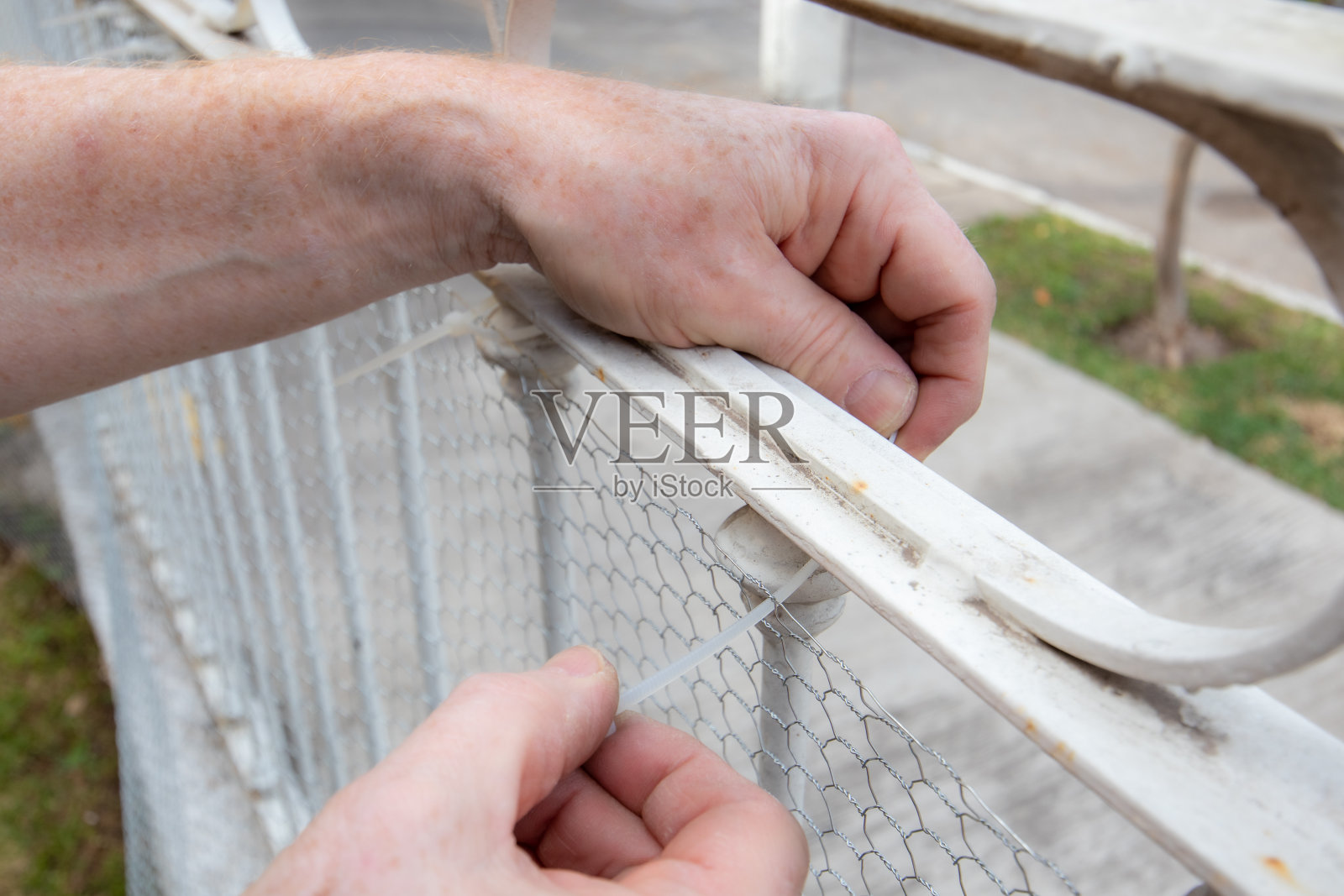 特写男性高级男子的手放置塑料电缆扎住金属网在栅栏上照片摄影图片