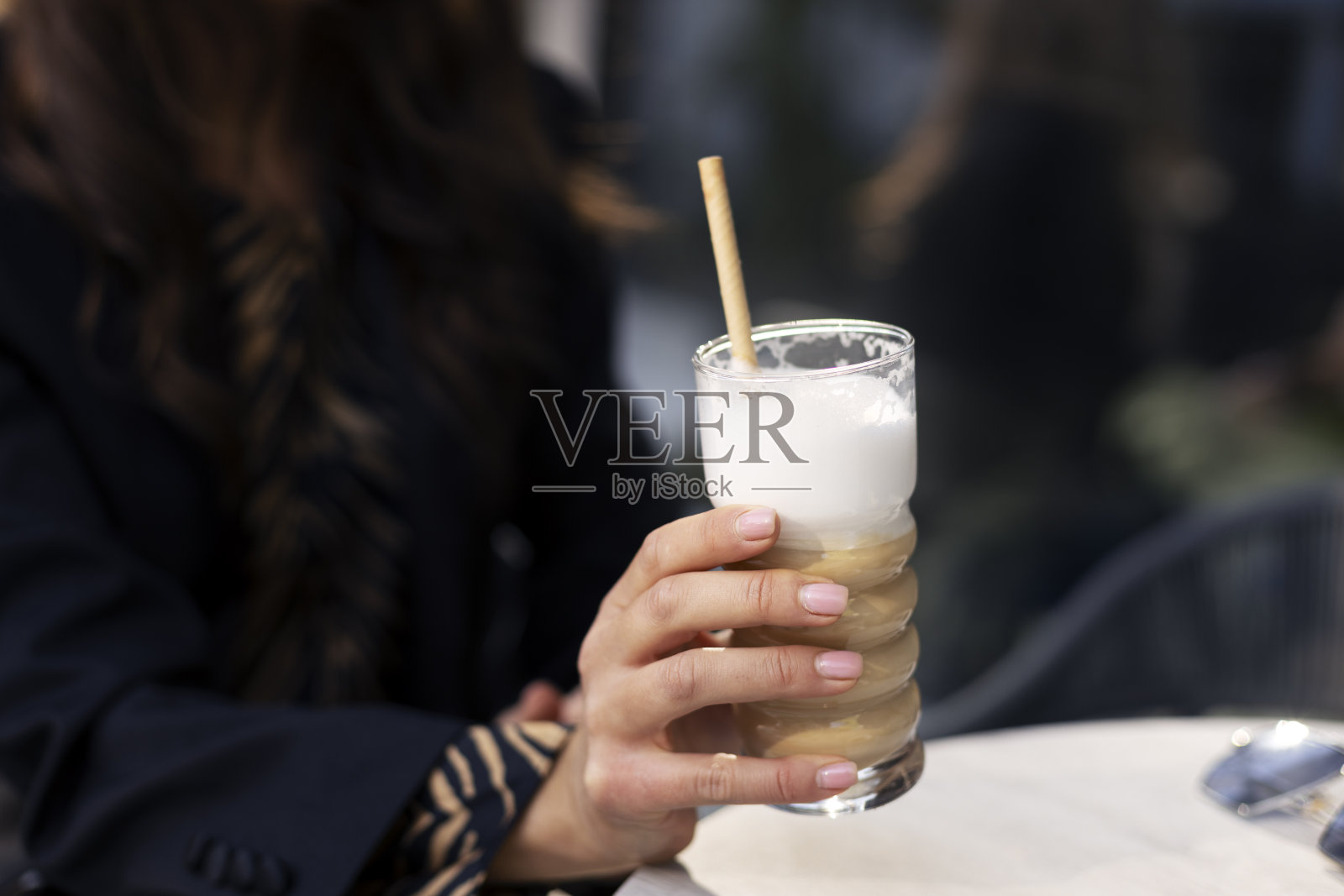 一个女人在桌子旁边拿着一个杯子，手里拿着一杯饮料。特写，一个咖啡馆或餐厅的女孩拿着咖啡饮料。照片摄影图片