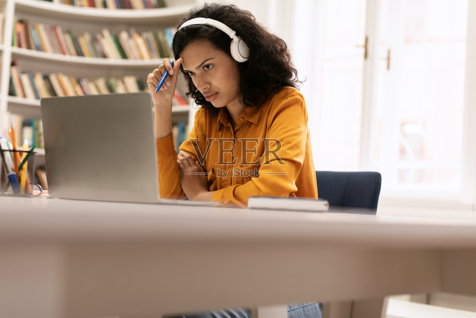 专注的混血女士在图书馆使用笔记本电脑和无线耳机在线学习，有复制空间照片摄影图片