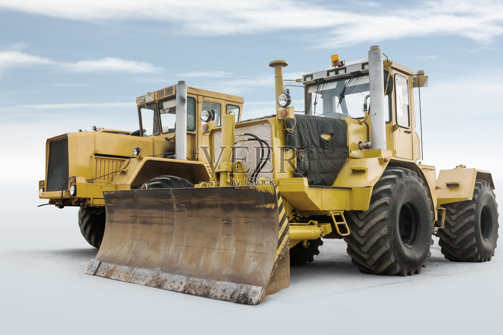 两辆黄色重型轮式拖拉机孤立在明亮的天空背景下照片摄影图片