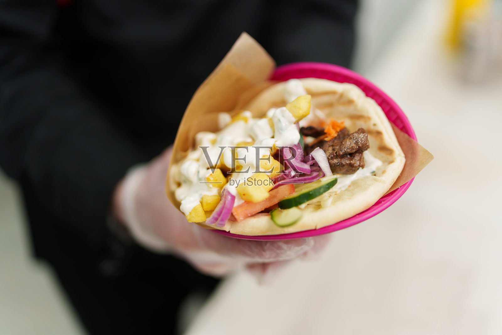 传统的希腊皮塔饼配烤肉，酸奶酱和新鲜蔬菜。厨师手里拿着新鲜的烤陀螺。照片摄影图片