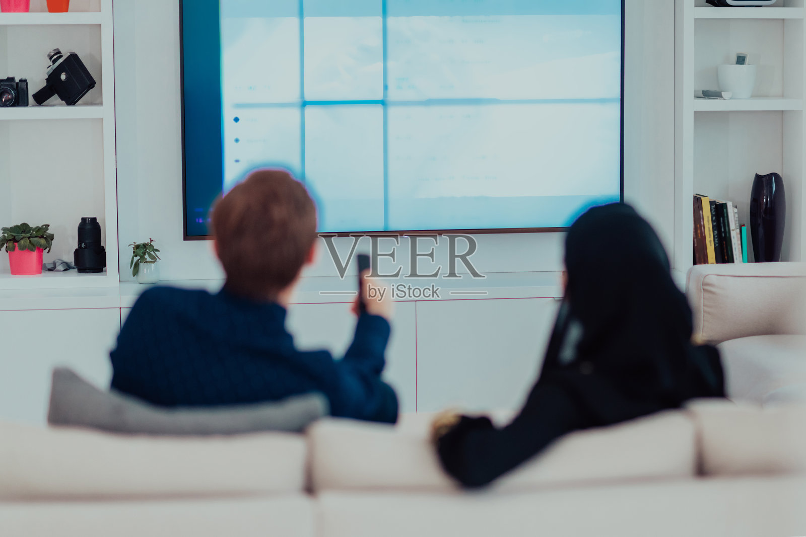 年轻的穆斯林夫妇妇女穿着伊斯兰头巾坐在沙发上看电视在斋月期间在现代家庭照片摄影图片