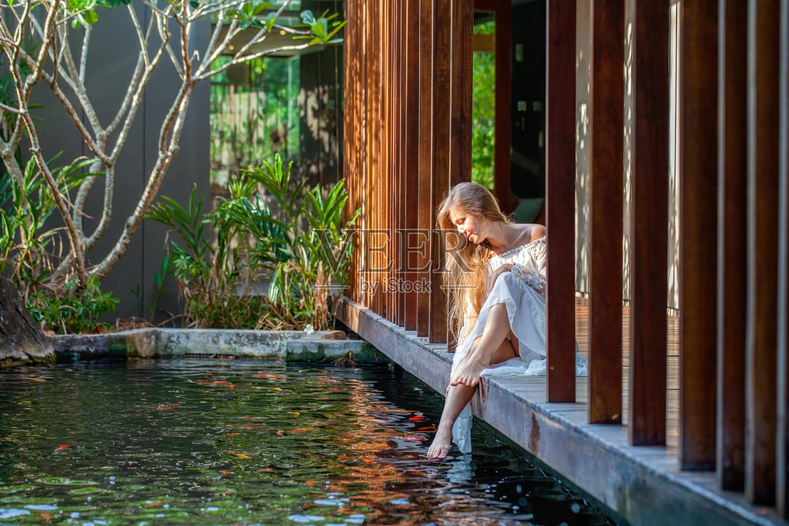 女人在白色连衣裙放松在豪华温泉与鱼塘照片摄影图片