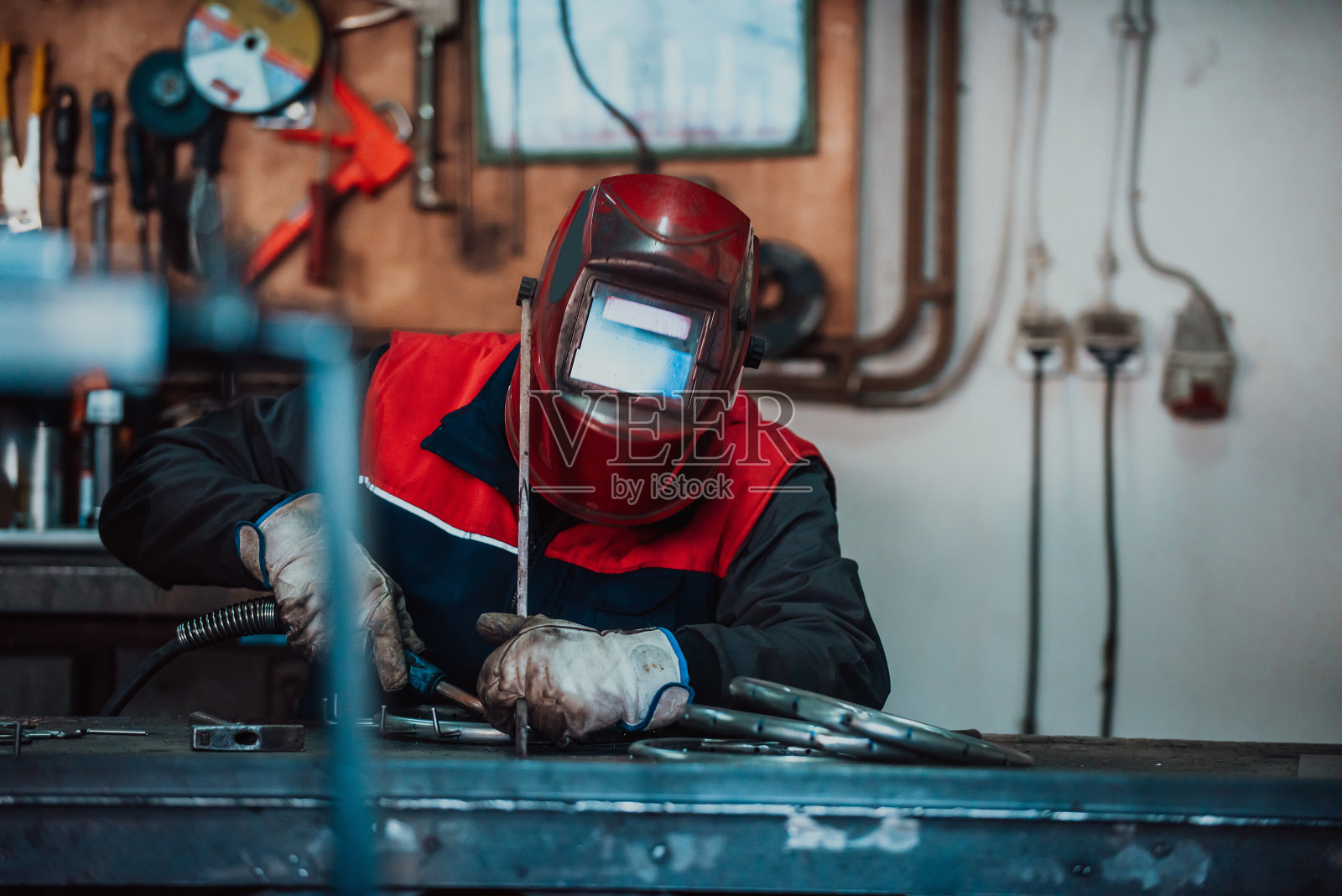 在工业车间，专业焊工穿着防护服，戴着面罩，与其他工人一起在工业台上焊接金属管道。照片摄影图片