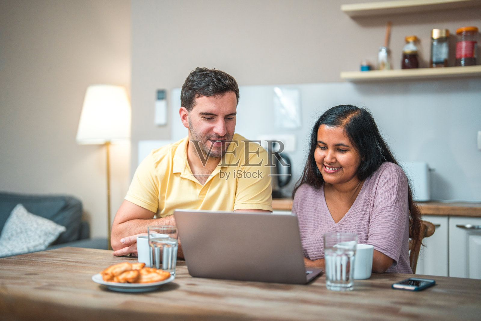 不同的夫妇在厨房里用笔记本电脑娱乐自己照片摄影图片