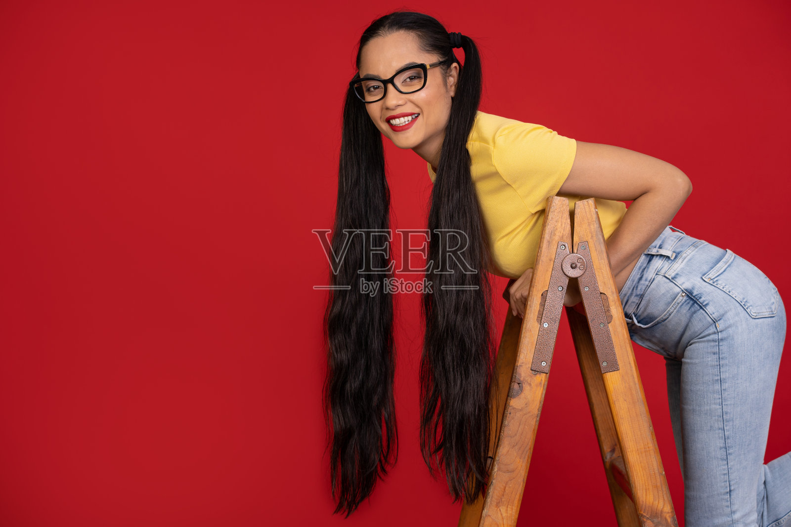 亚洲女性爬上梯子，在红色背景前摆姿势照片摄影图片