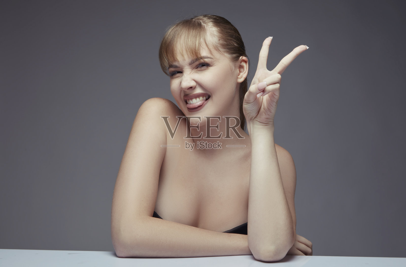 美丽的年轻女子的肖像伸出她的舌头，同时做和平手势与她的手。照片摄影图片