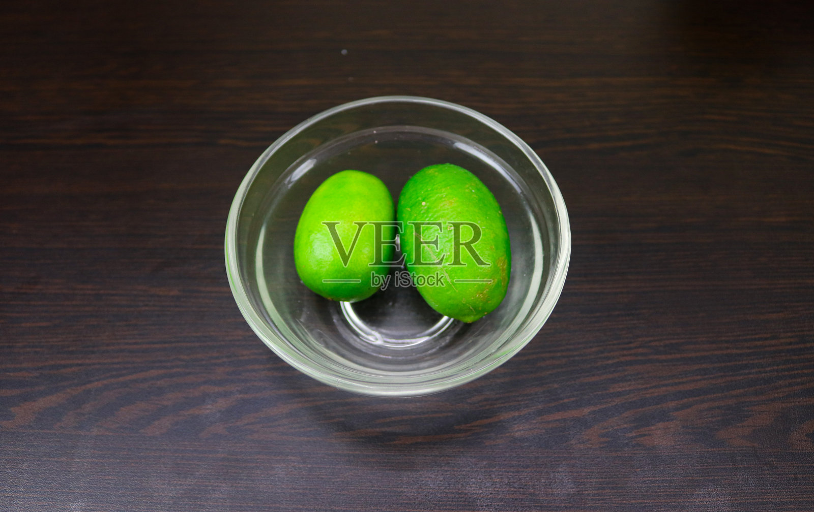 顶部视图的绿色柠檬在玻璃碗上的木制背景。照片摄影图片