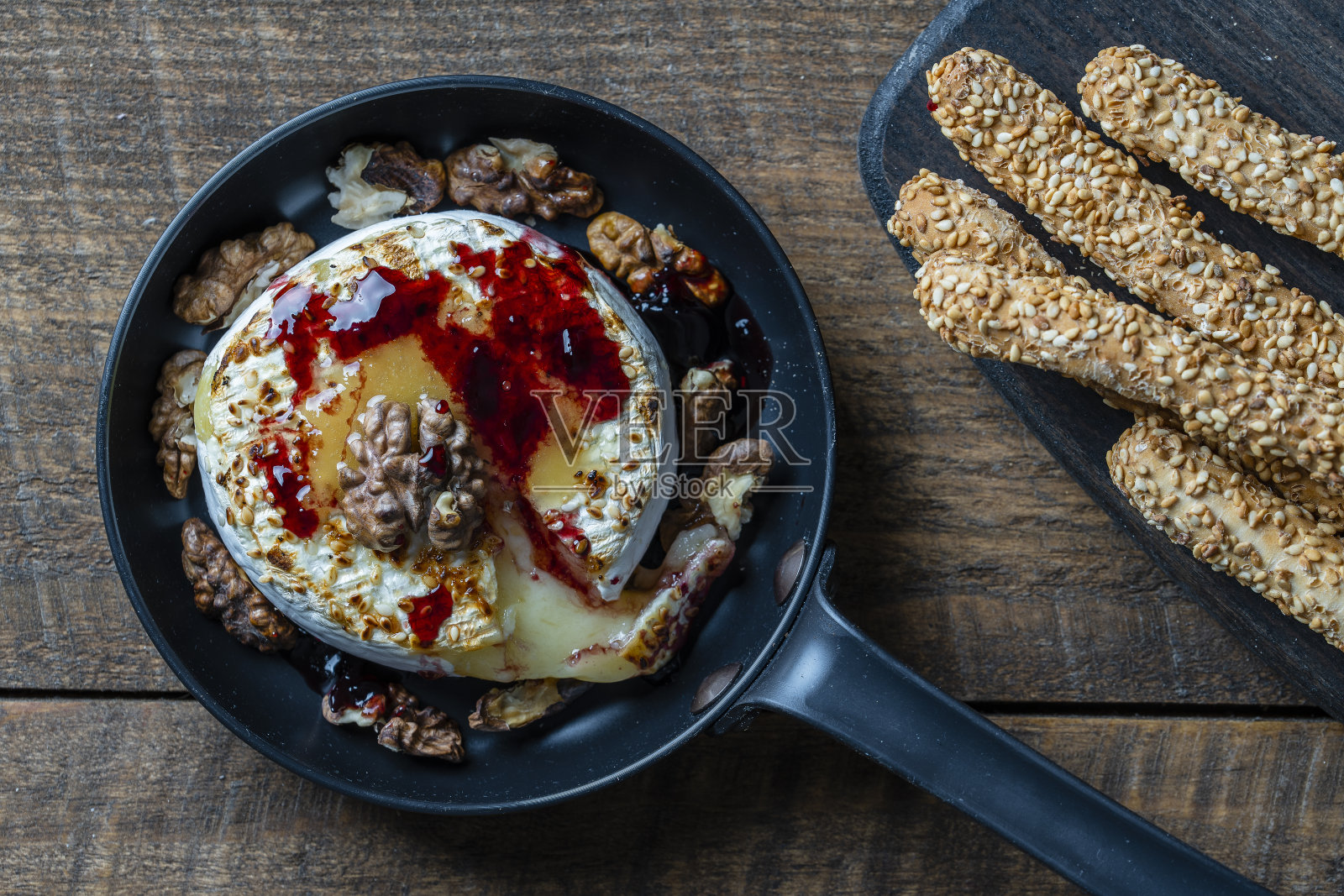 在煎锅上烤卡门贝尔奶酪，核桃，蜂蜜，果酱和面包棒与芝麻在木桌背景，特写，俯视图照片摄影图片