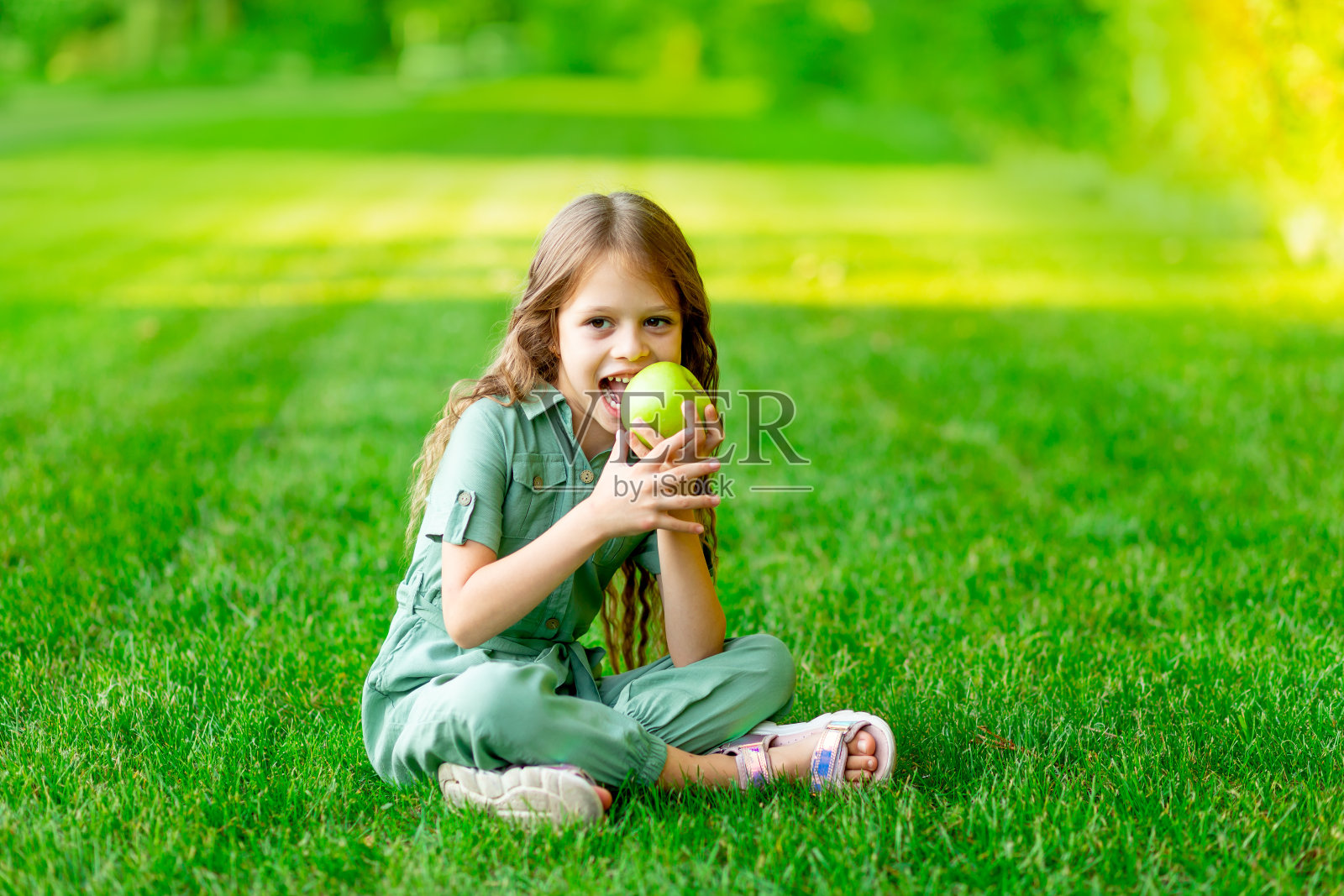 夏天的草坪上，快乐的女婴用健康的牙齿咬着绿苹果，在草地上微笑，有文字的空间照片摄影图片