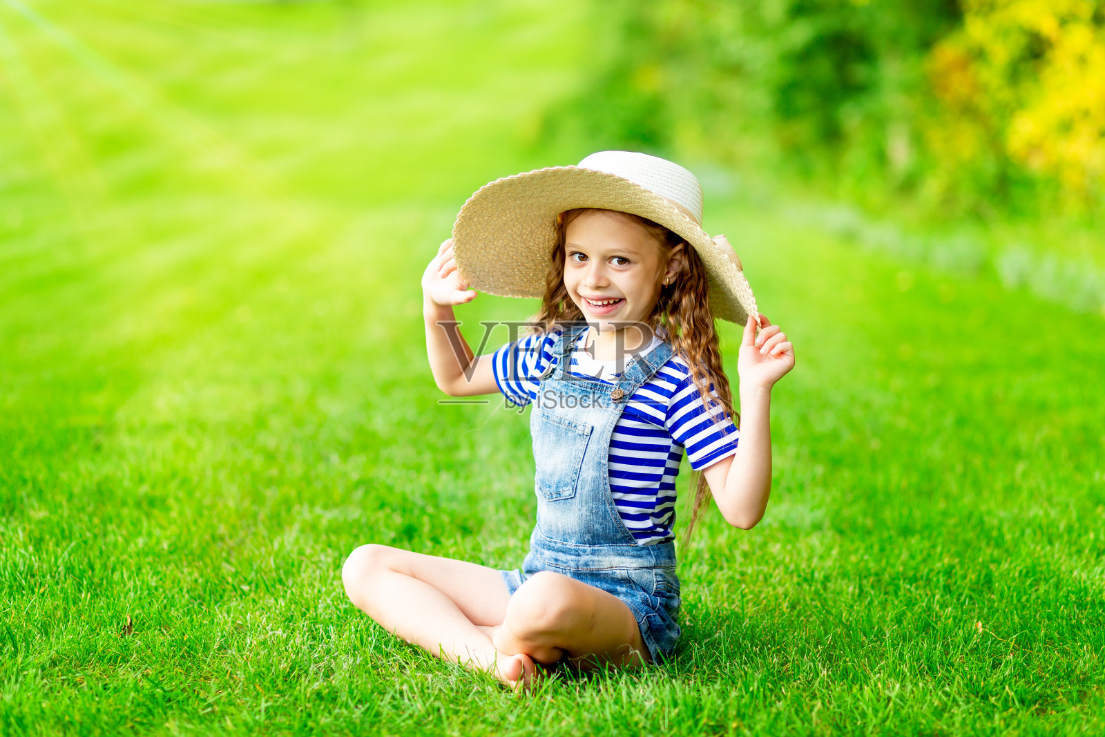 有趣的女婴在夏天的草坪上戴着大草帽，在绿茵茵的草地上欢天喜地，有文字的空间照片摄影图片