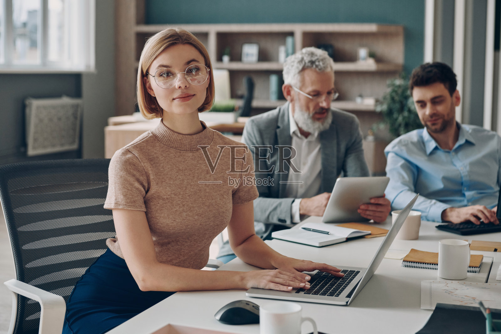 三个商人在办公室一起工作，而年轻女子看着相机照片摄影图片