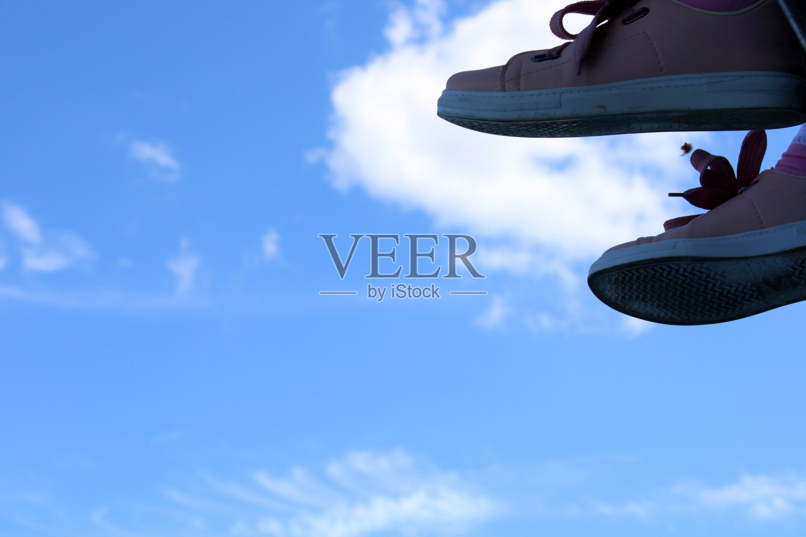 一双鞋子挂在一根杆子上，背景是天空。照片摄影图片