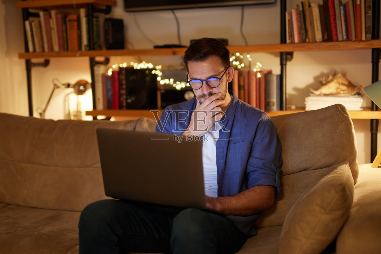 忧心忡忡的中年男子晚上坐在沙发上使用笔记本电脑照片摄影图片