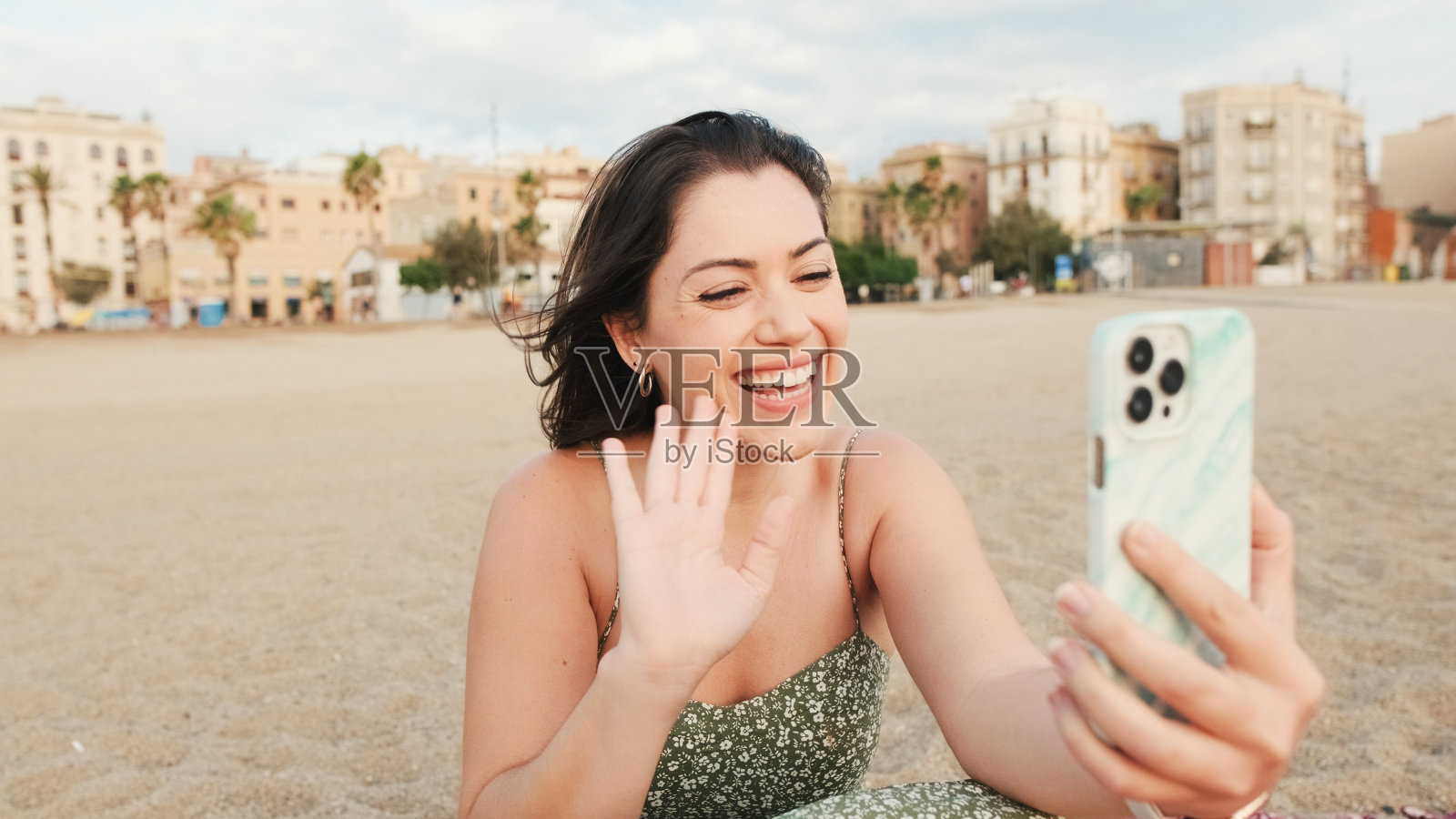 年轻女子坐在沙滩上，用手机，视频通话照片摄影图片