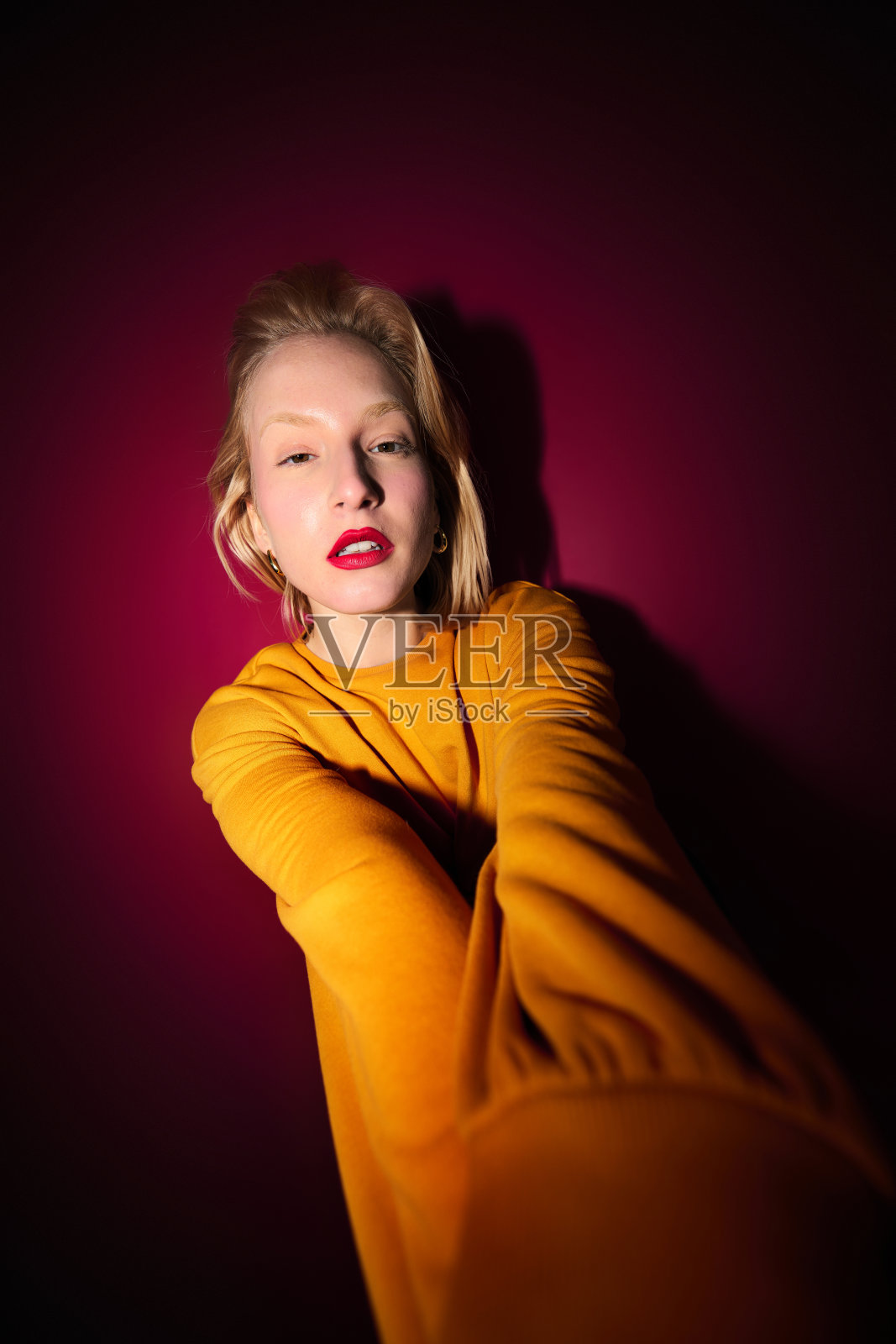 一个严肃的金发女孩把手伸向相机，看着它。洋红色万岁。照片摄影图片