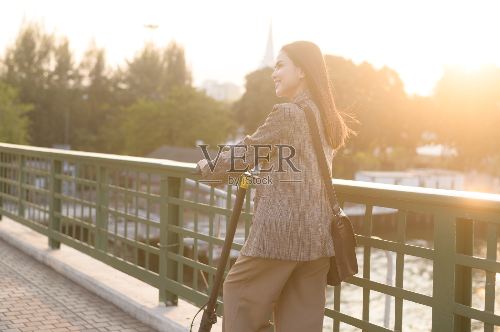 在现代城市背景下，年轻的商业女性用电动滑板车在桥上工作的肖像照片摄影图片