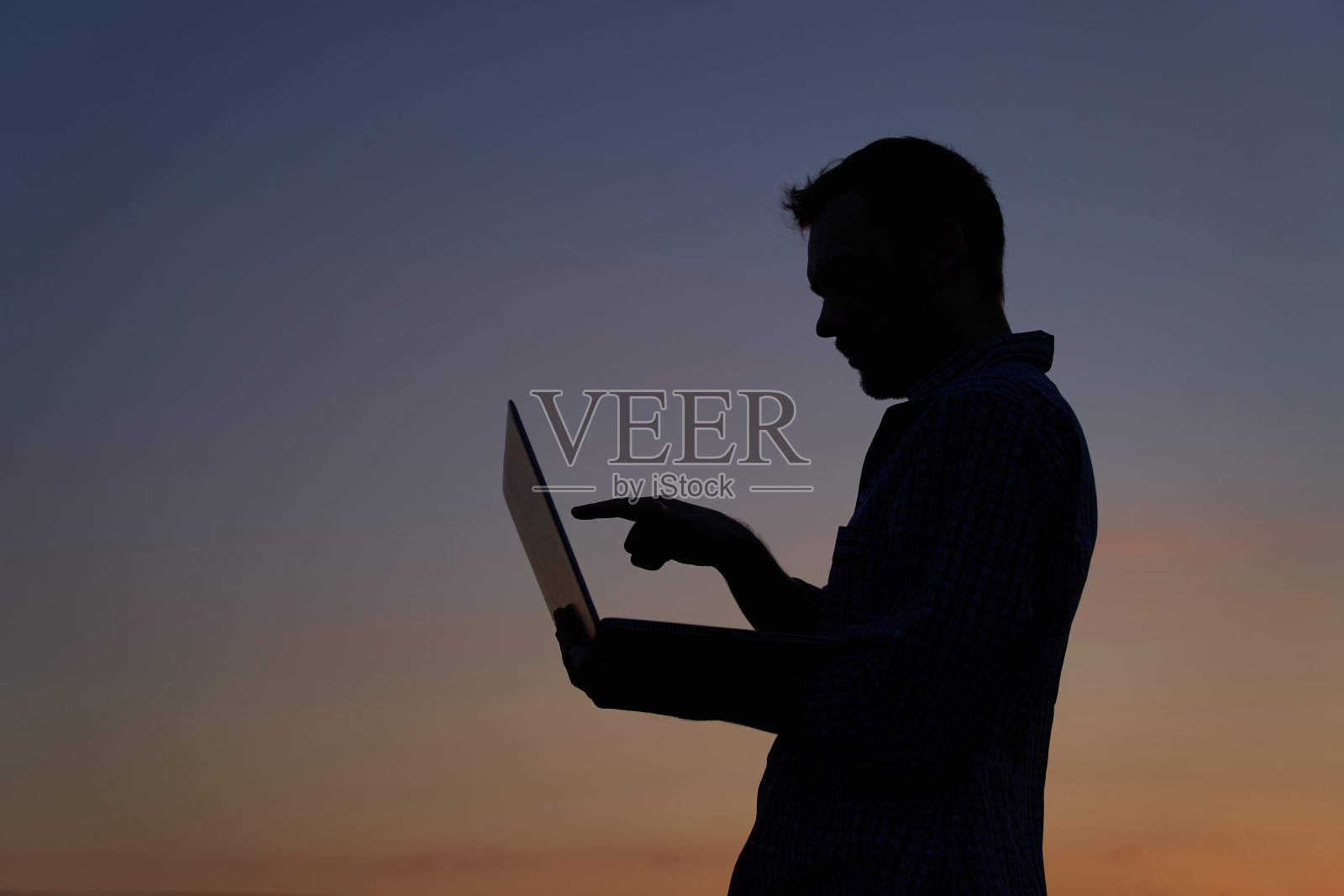 男子剪影使用笔记本电脑在户外日落，会议和指向屏幕照片摄影图片