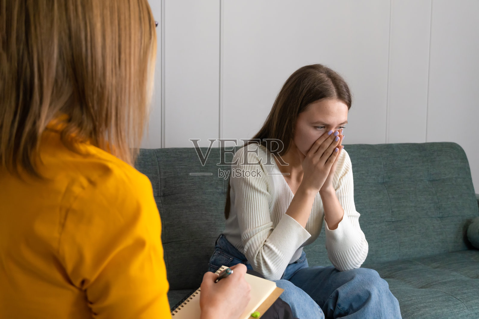 一个悲伤的女人坐在沙发上，双手捂着脸去看心理治疗师。心理医生和客户在一起。心理学家背后的照片照片摄影图片