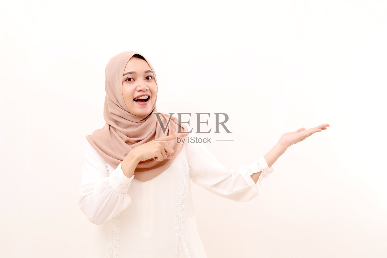 惊奇的年轻亚洲穆斯林妇女站在肖像，而提出和指向空白空间上的东西照片摄影图片