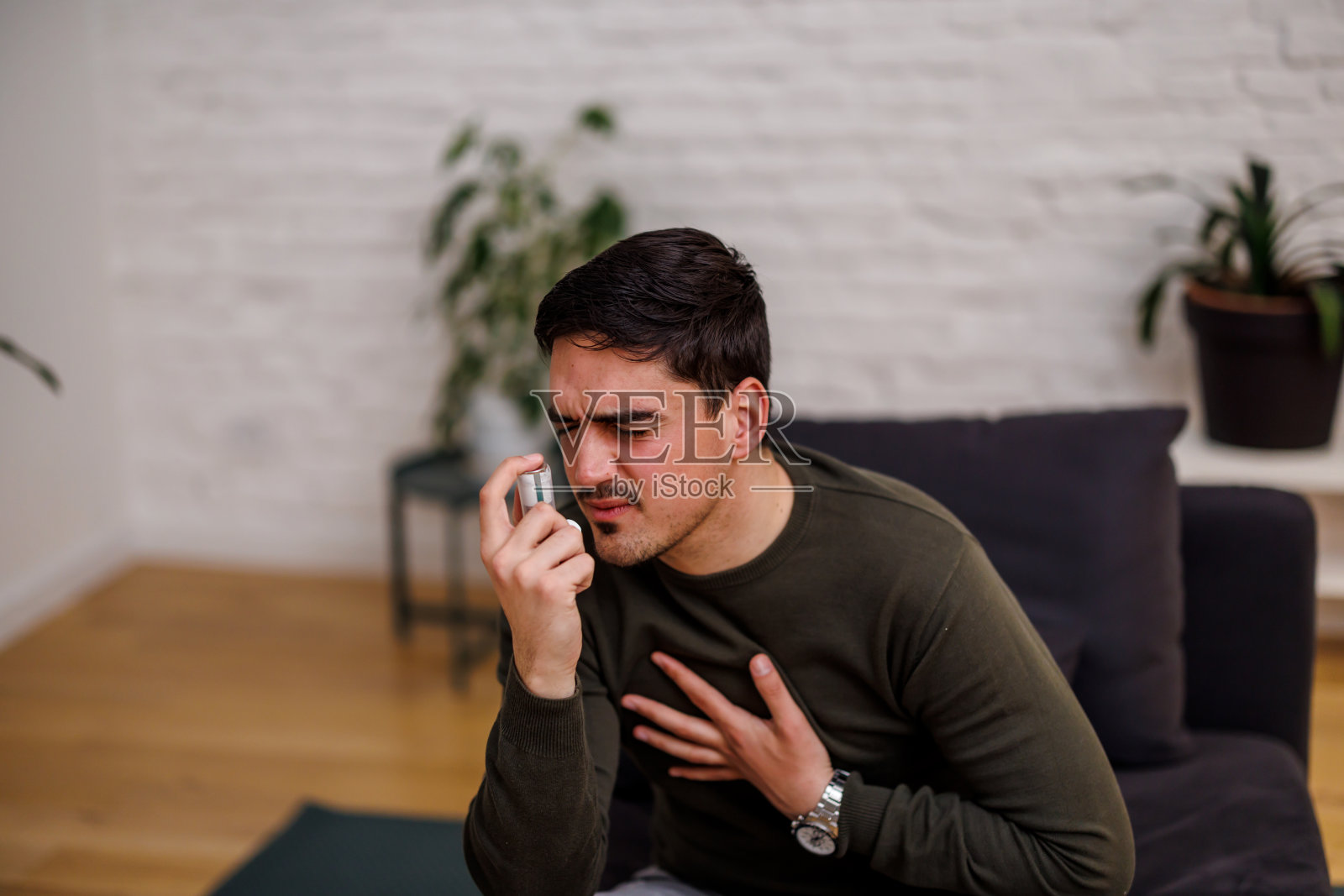 一个患有哮喘的年轻男人正在家里使用气雾剂吸入器照片摄影图片