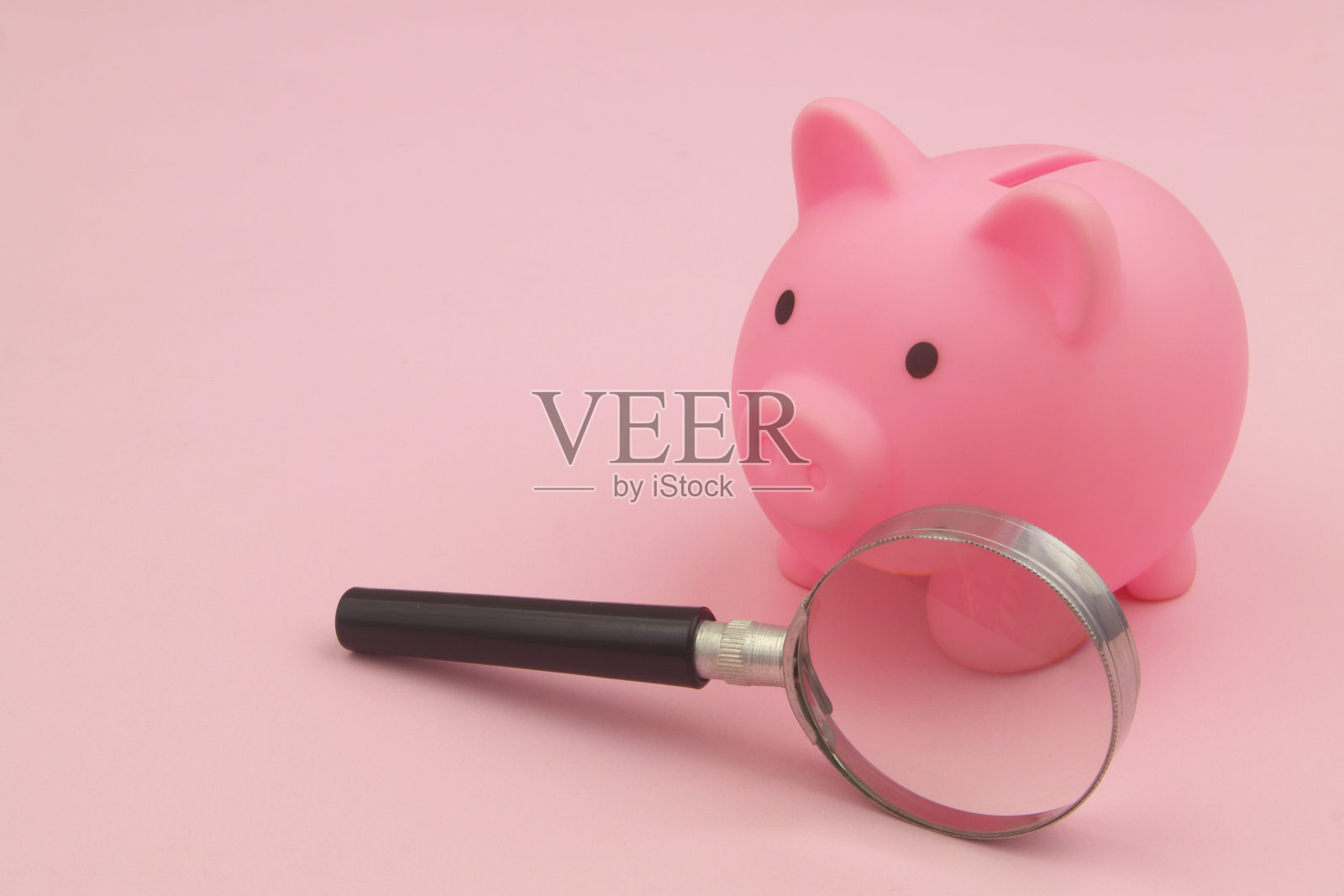 粉红色背景上的放大镜和粉色储蓄罐。文本复制空间。照片摄影图片