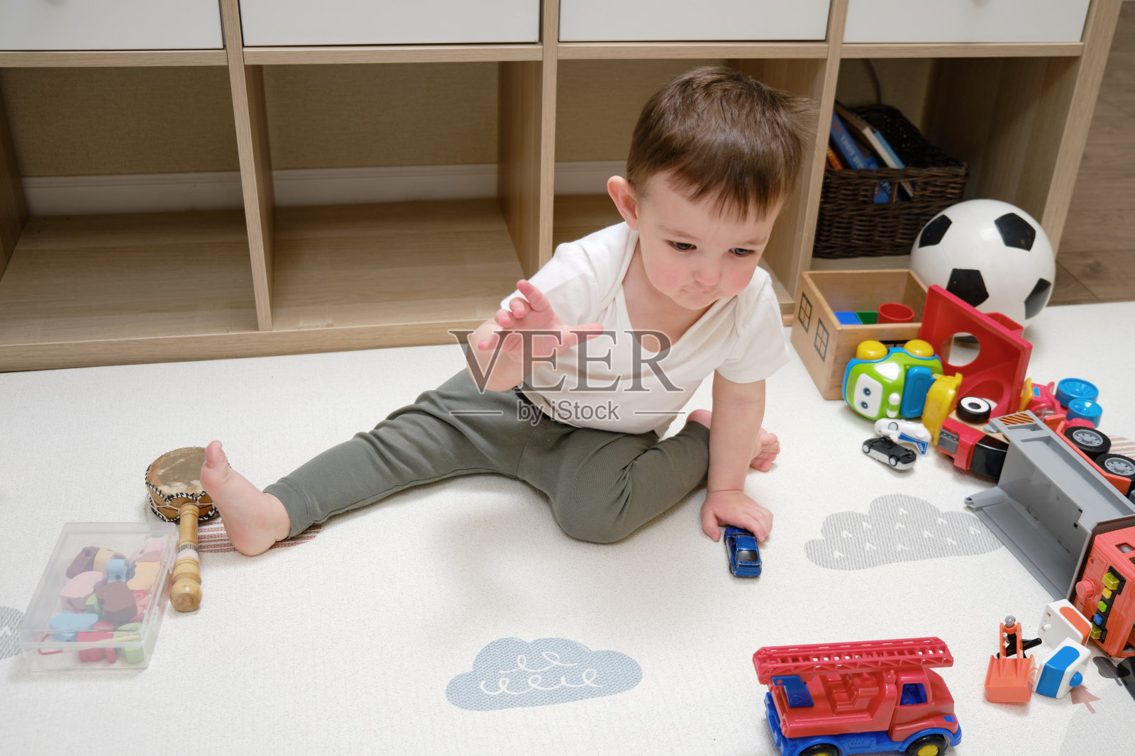 蹒跚学步的小男孩坐在育儿室的地毯上玩汽车。一个小孩在玩玩具。一岁八个月大的孩子照片摄影图片