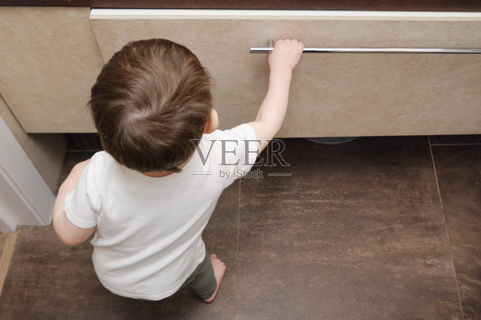 蹒跚学步的婴儿在家庭浴室里拿出一个物品抽屉。一个小孩在浴室的壁橱里摸索。一岁八个月大的孩子照片摄影图片