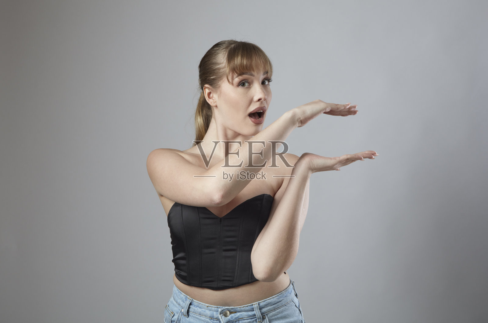 年轻的金发女人看着相机惊讶，而提出什么是她在她的手掌。照片摄影图片