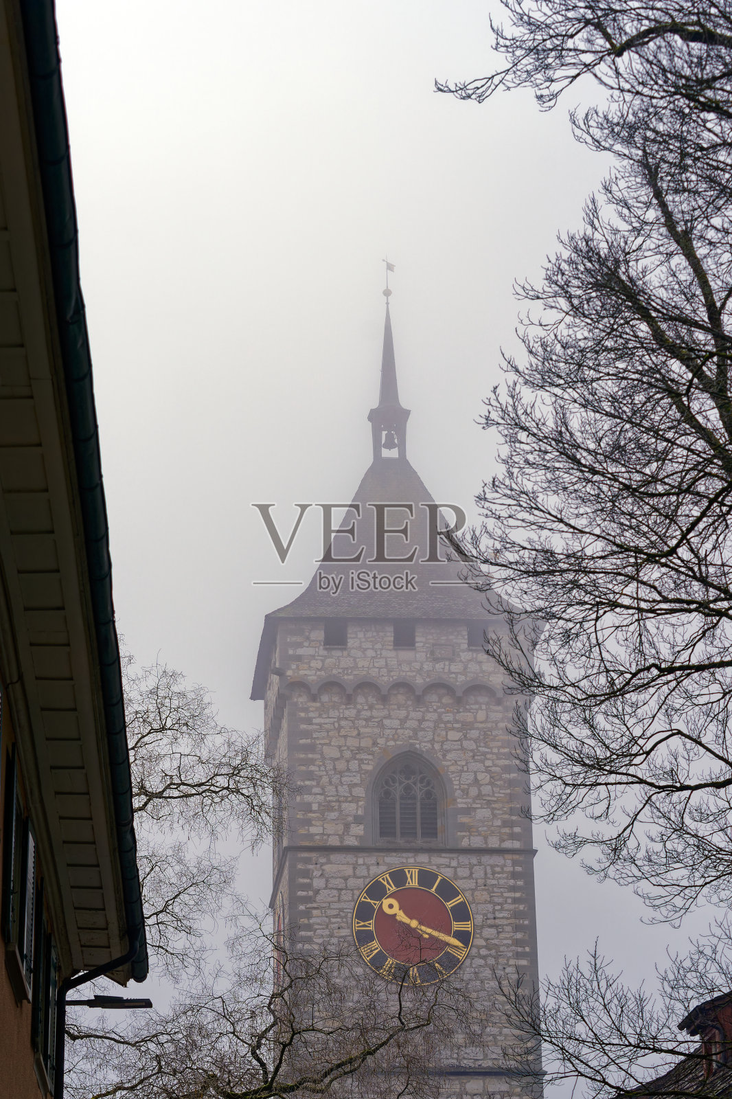 在一个雾蒙蒙的冬日，瑞士沙夫豪森老城区，圣约翰教堂的石制教堂塔和钟面。照片摄影图片