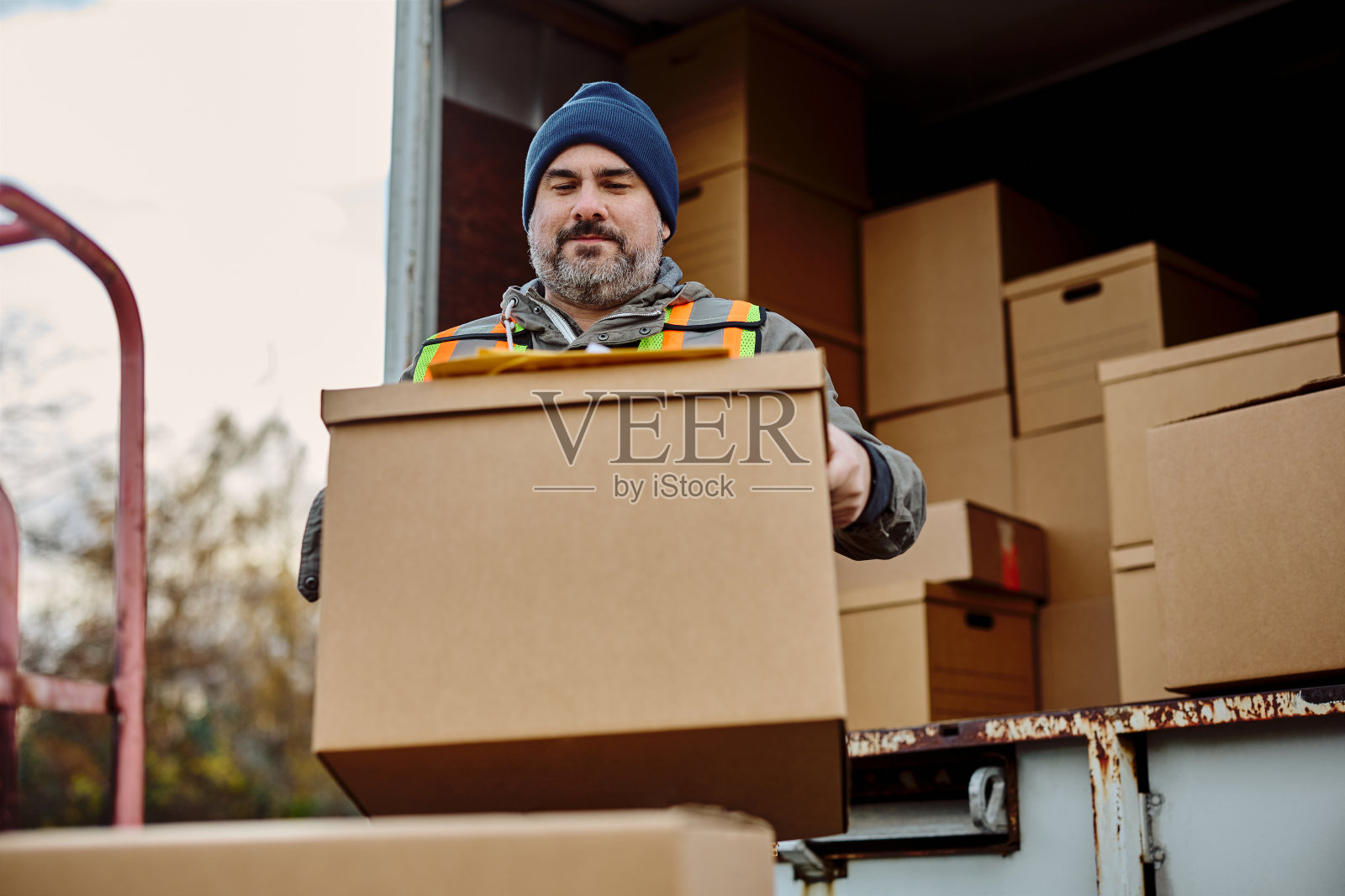 微笑的快递员从卡车上卸下纸箱。照片摄影图片