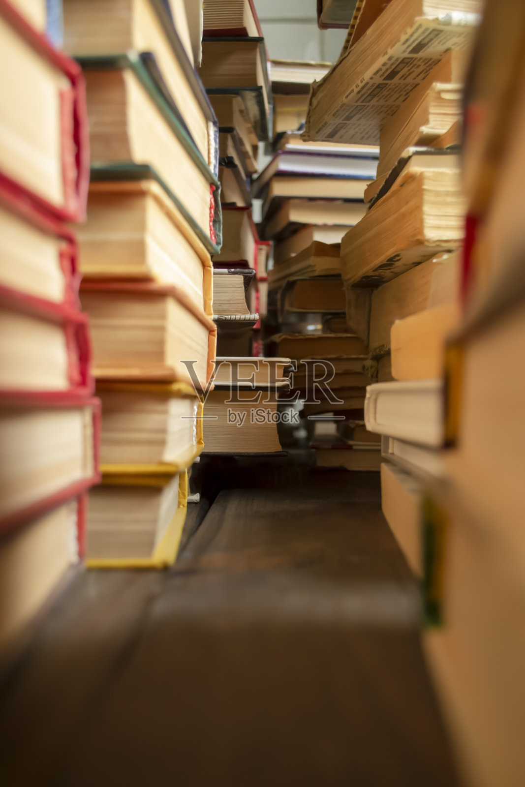 一排排的书放在木地板上。许多教科书堆放在一个地方。很多书都堆在一起了。一排旧书之间的过道。照片摄影图片