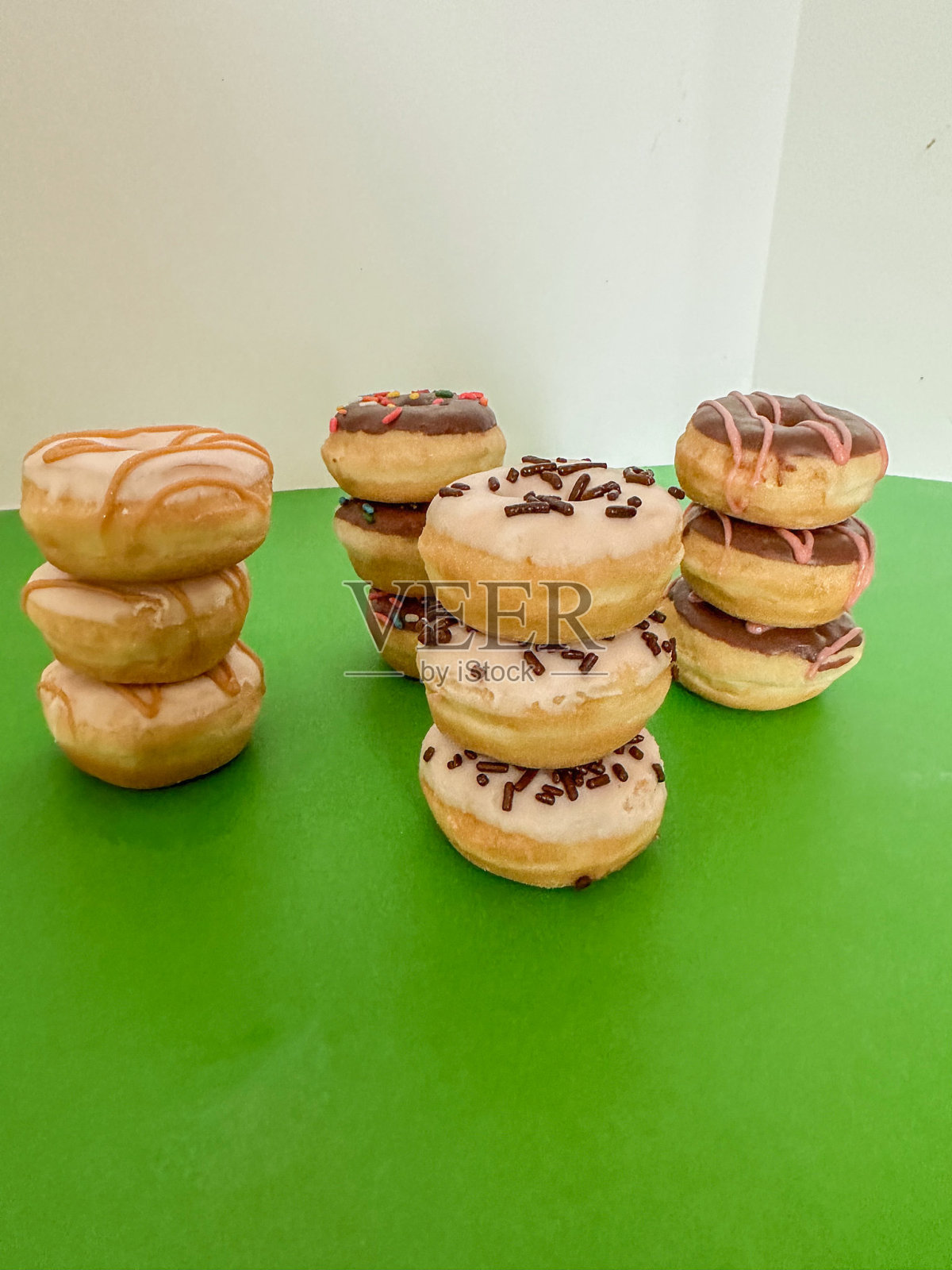 九个圆形迷你甜甜圈堆叠在绿色背景上照片摄影图片