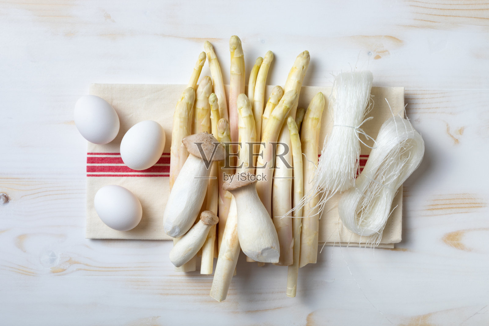 白色木桌上摆着一串生芦笋、鸡蛋、蘑菇和干米粉。俯视图，复制空间照片摄影图片