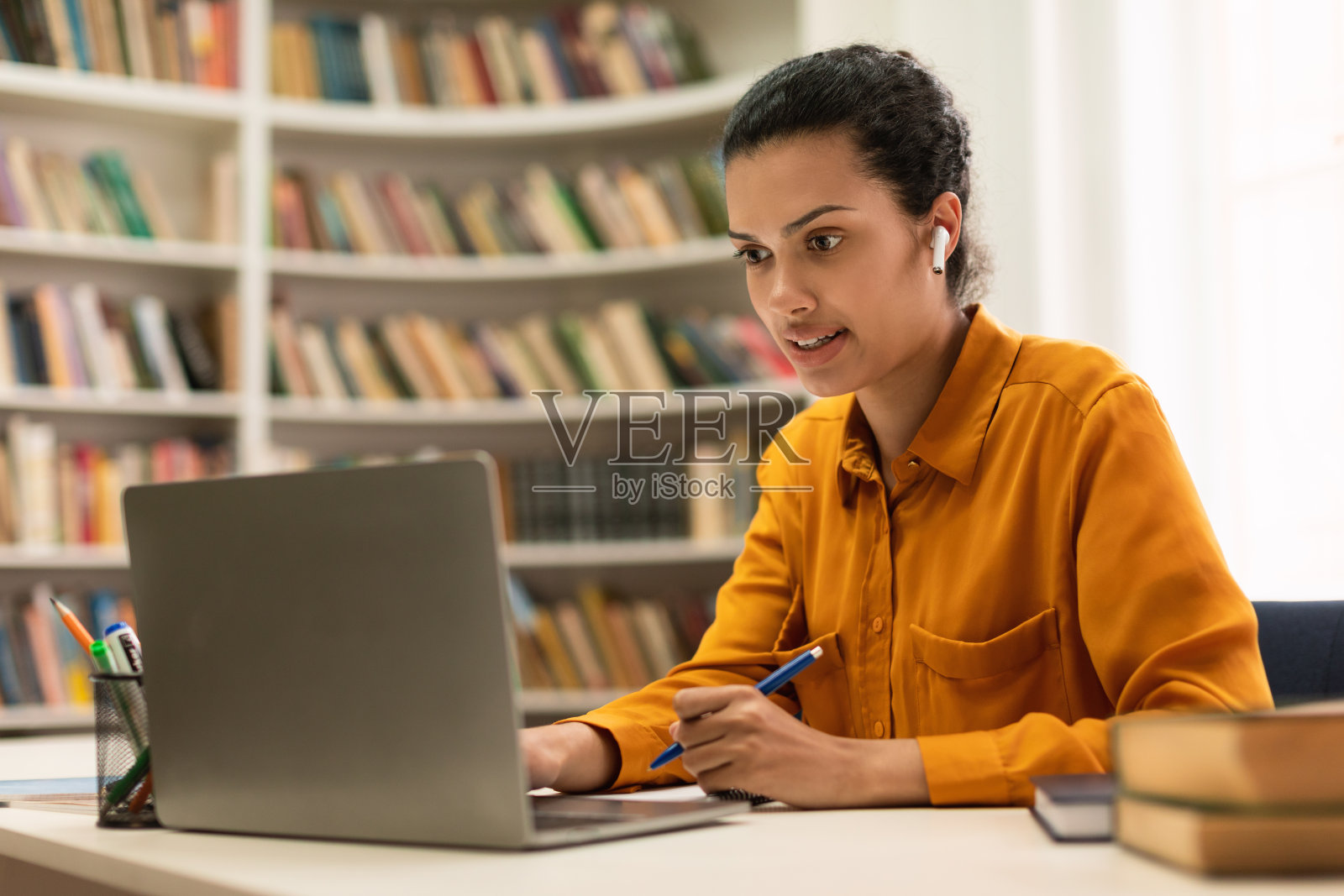 远程教育概念：混血年轻女性在图书馆的桌旁使用笔记本电脑观看讲座或网络研讨会照片摄影图片