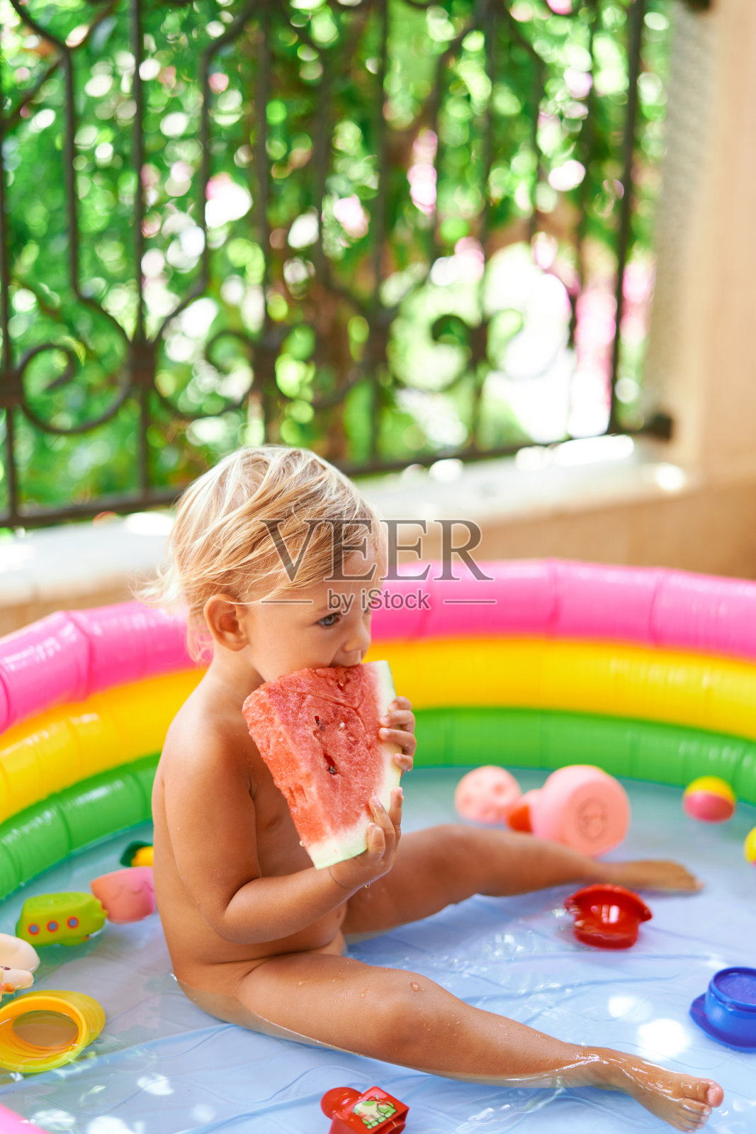 小女孩坐在阳台的充气泳池里吃西瓜照片摄影图片